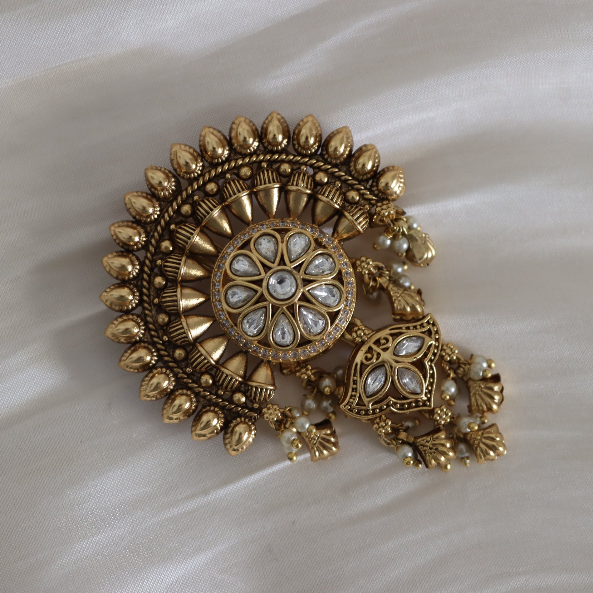 Decorative gold brooch with pearl-like stones on a white fabric background