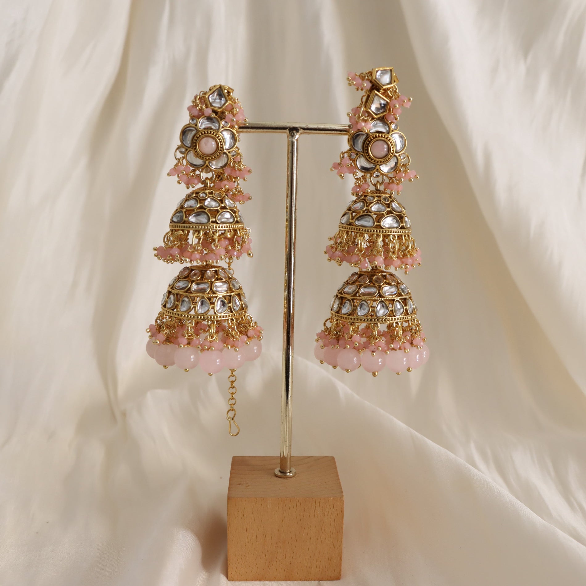 Ornate earrings with pink stones on a stand against a white fabric background