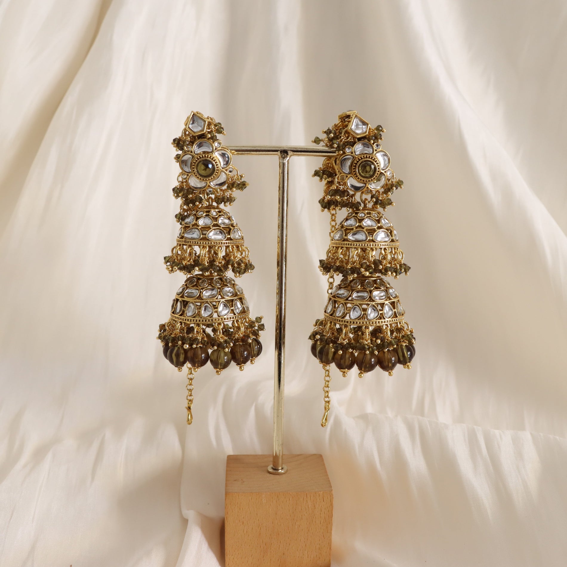 Ornate gold earrings on a stand against a white background