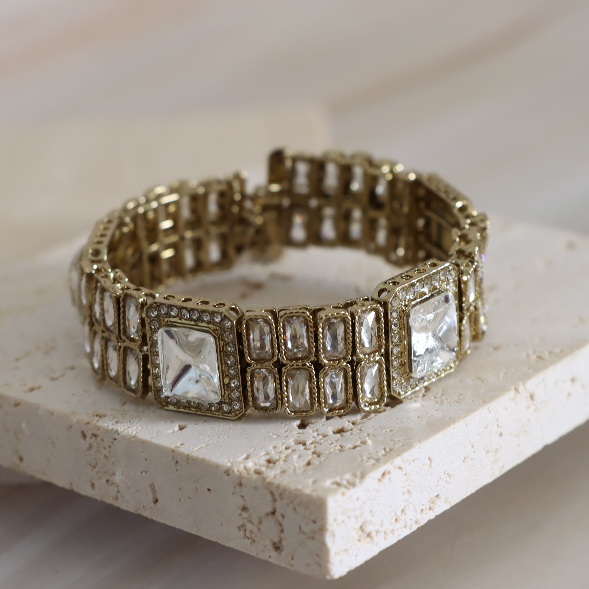 Gold bracelet with square gemstones on a light stone surface