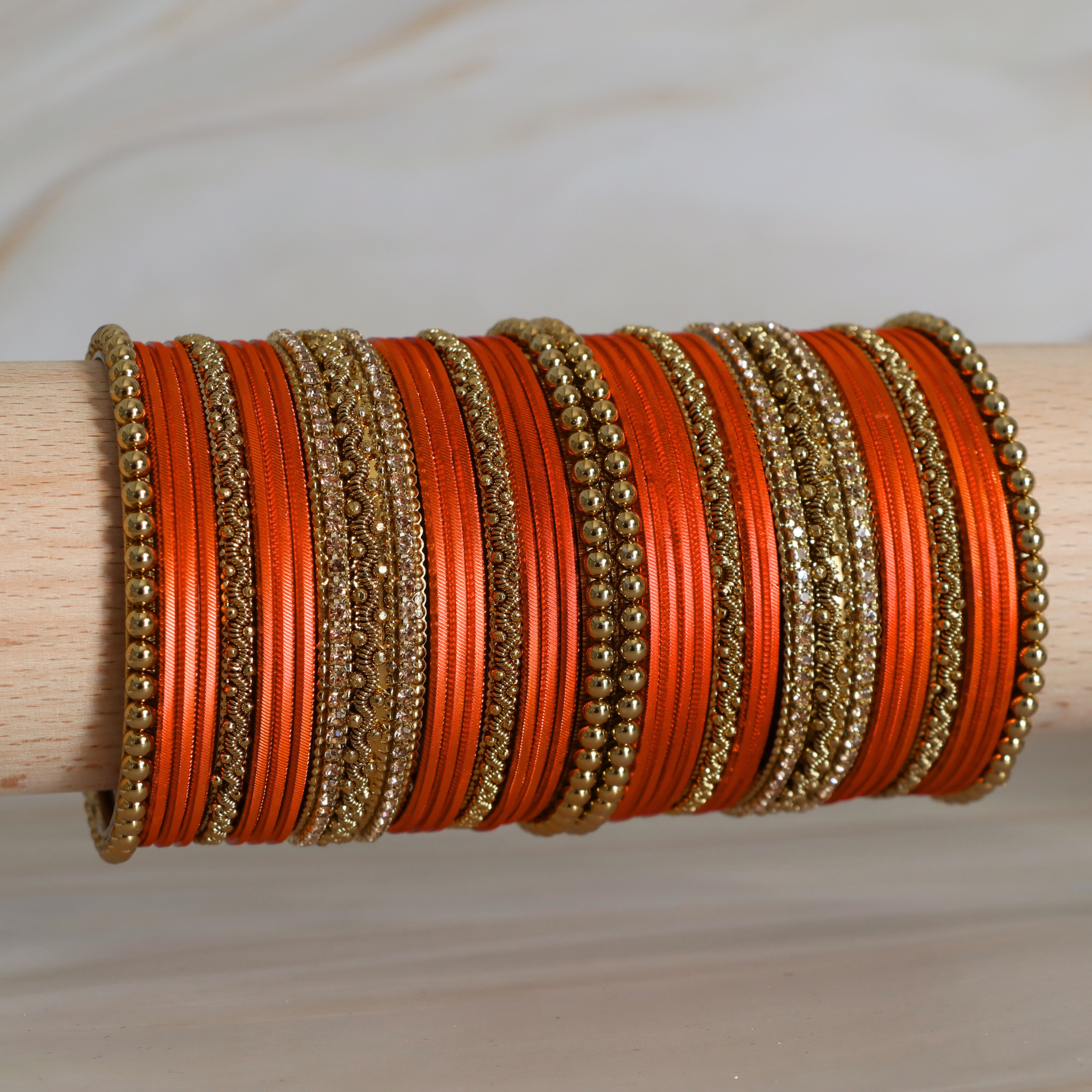 Stack of orange and gold bangles on a wooden stick against a neutral background