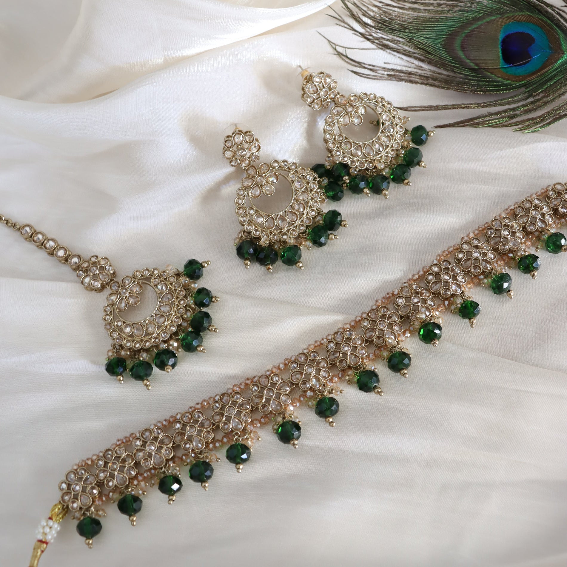 Jewelry set with green beads and gold accents on a white fabric background