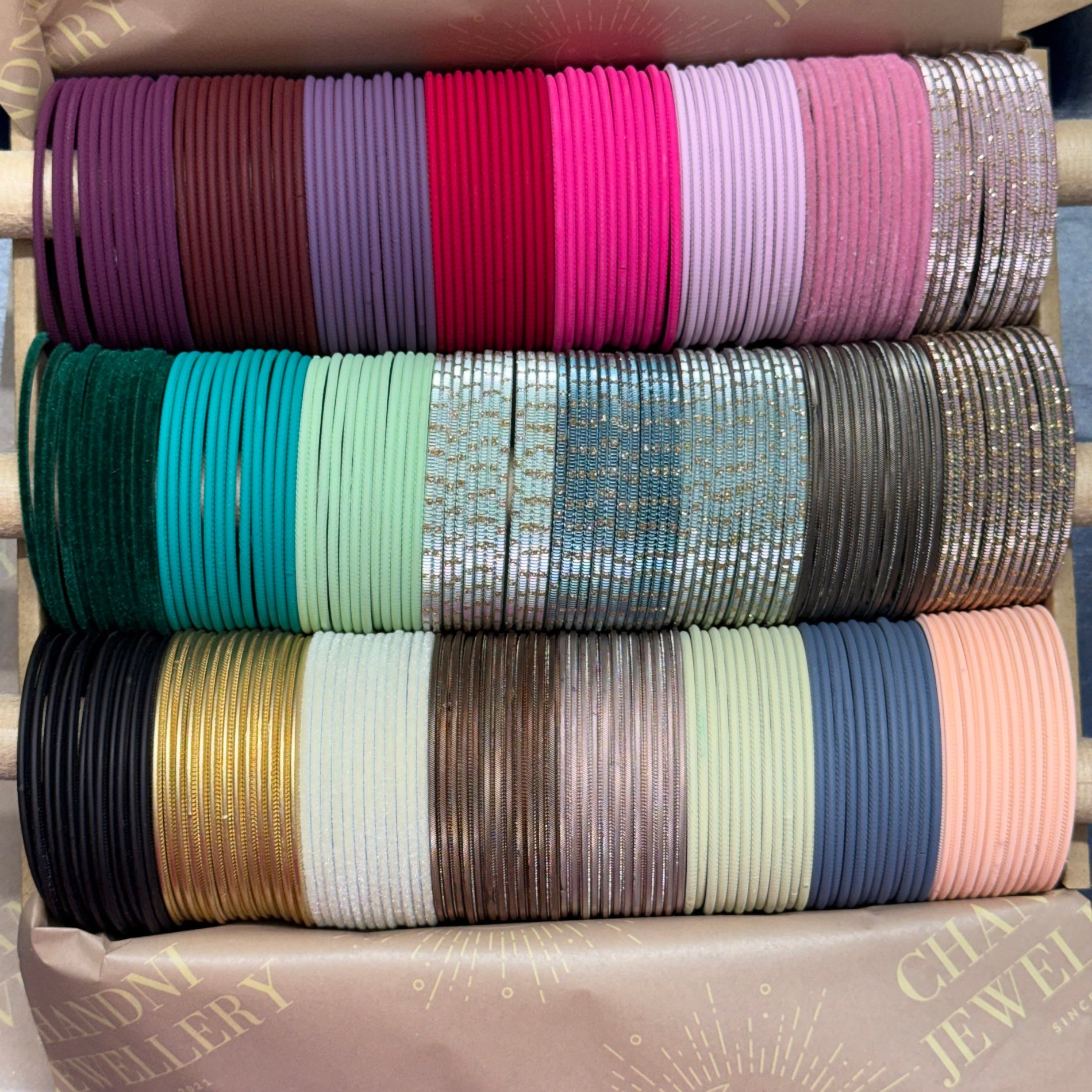 Stack of colorful bangles in various patterns and colors on a branded jewelry box.