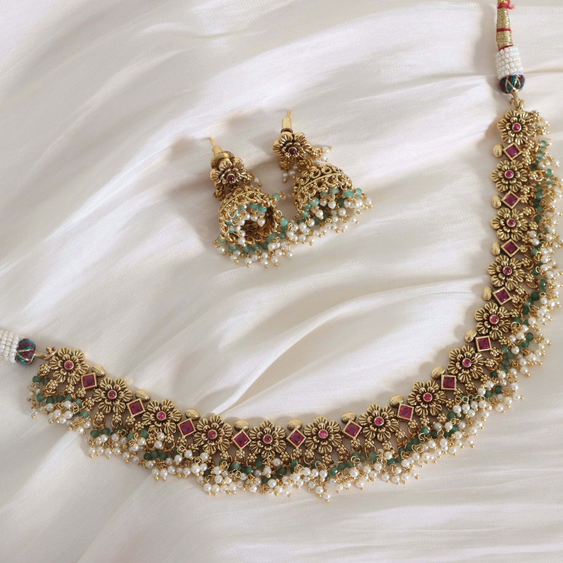 Ornate necklace and earrings set on a white fabric background