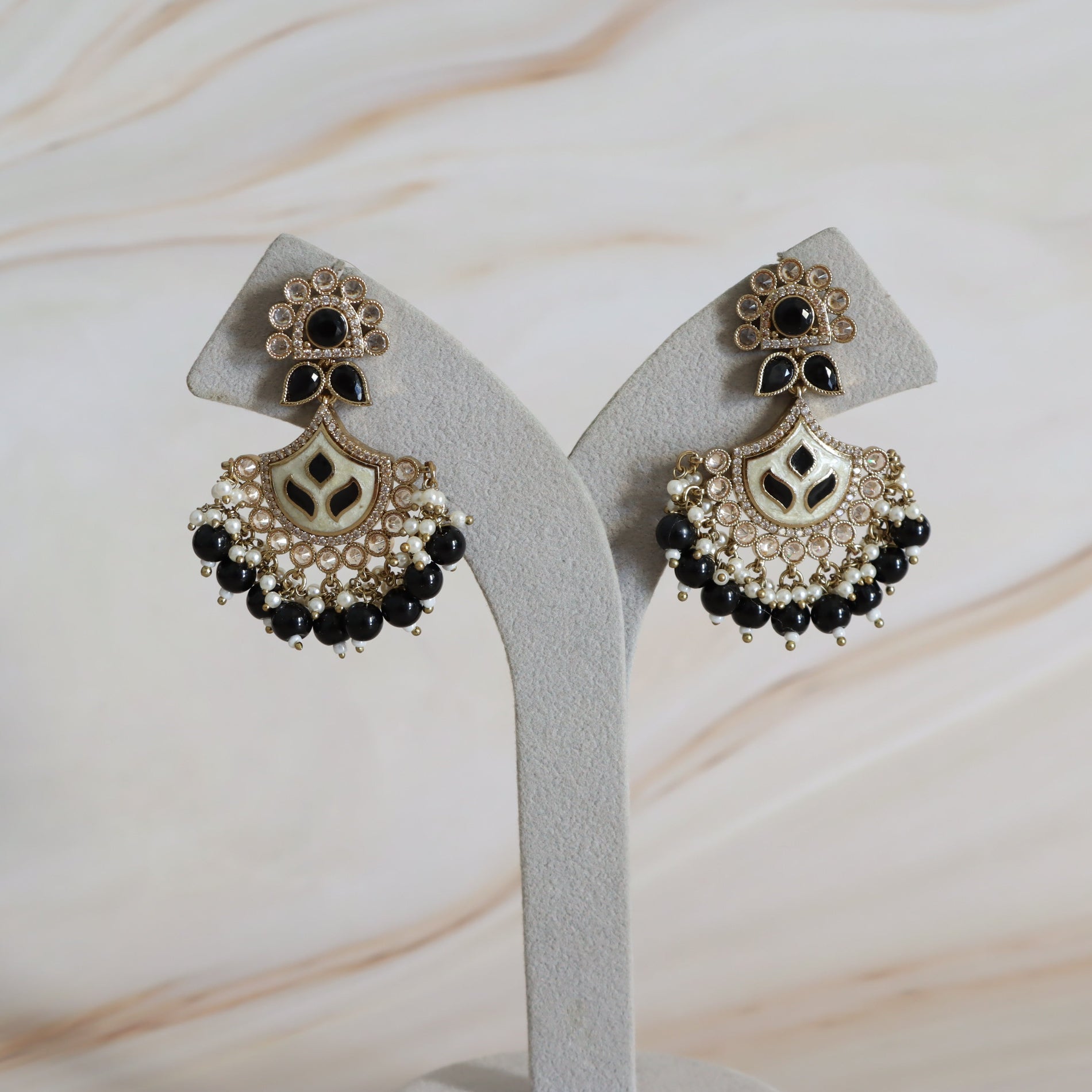 Pair of ornate earrings with black and gold details on a white stand against a marble background.