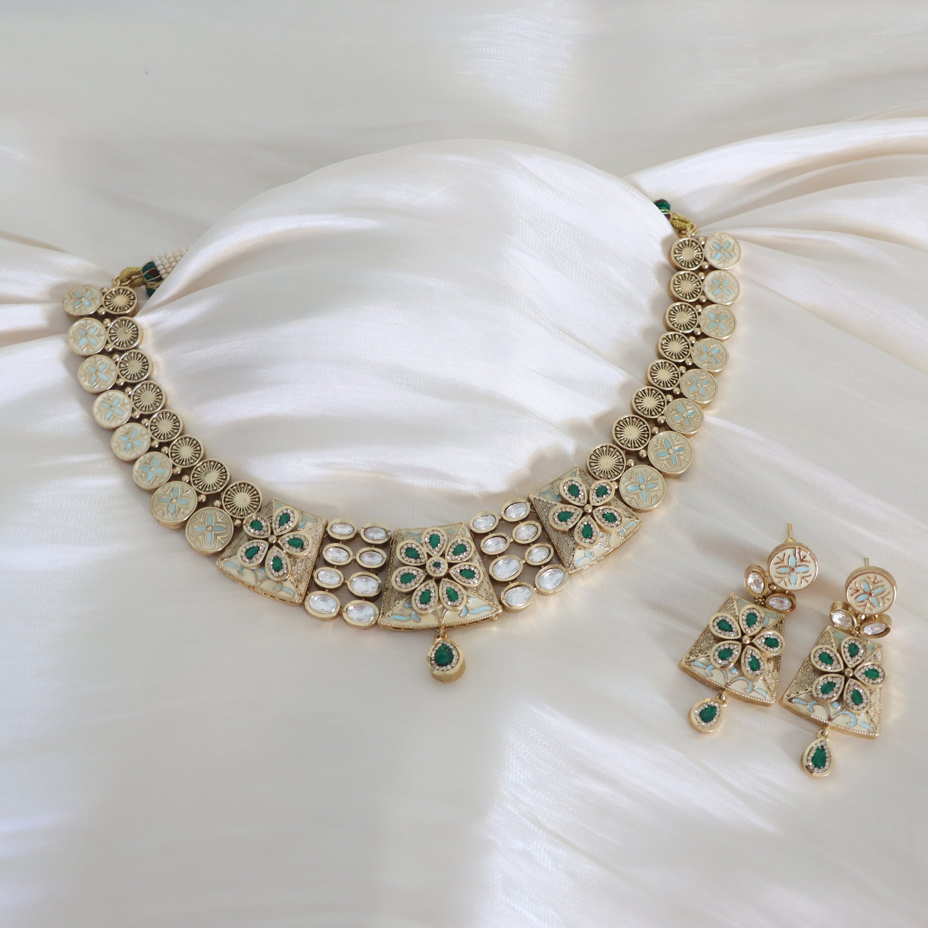 Gold necklace with green gemstones on a white fabric background