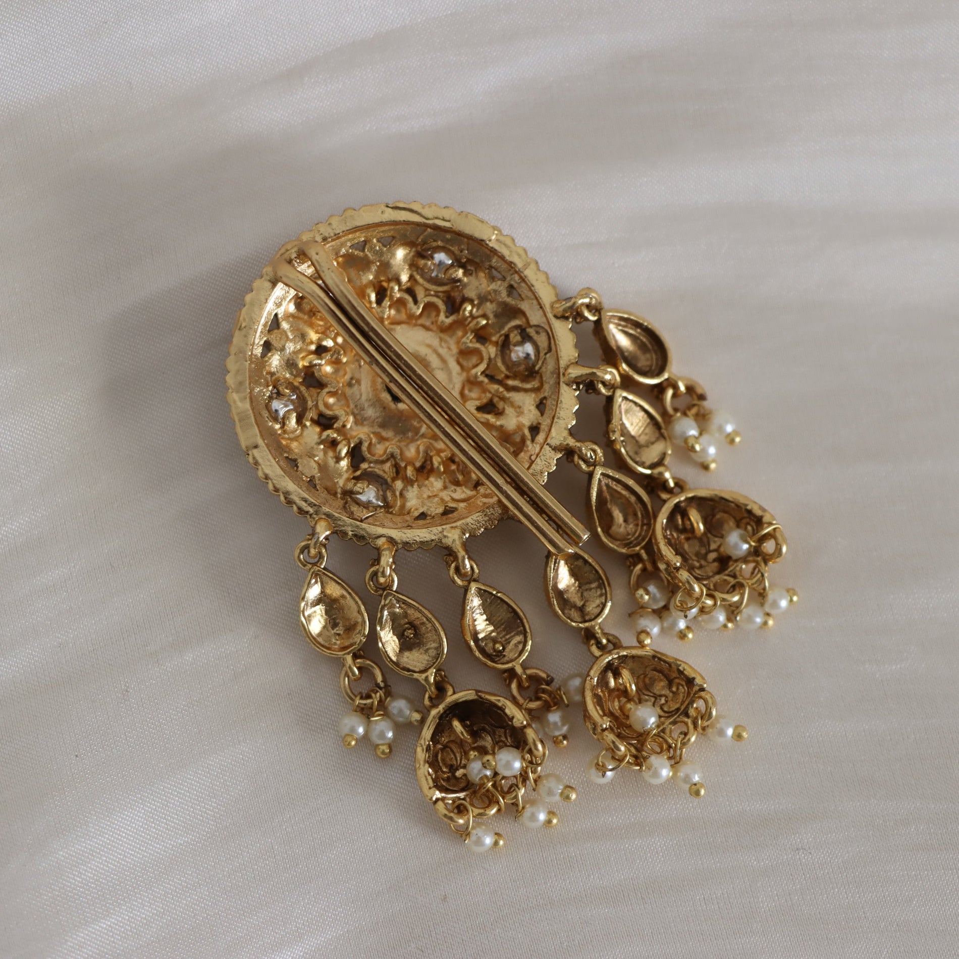 Gold brooch with pearl-like stones on a white fabric background