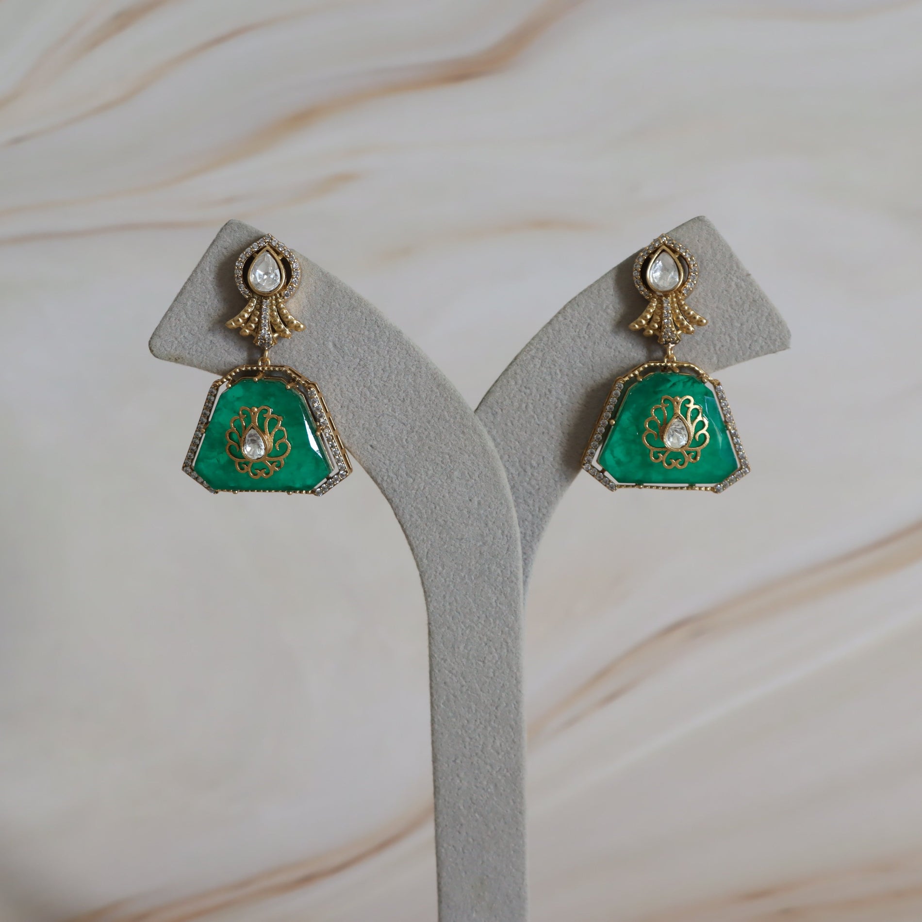 Pair of green earrings with gold accents on a gray stand against a beige background