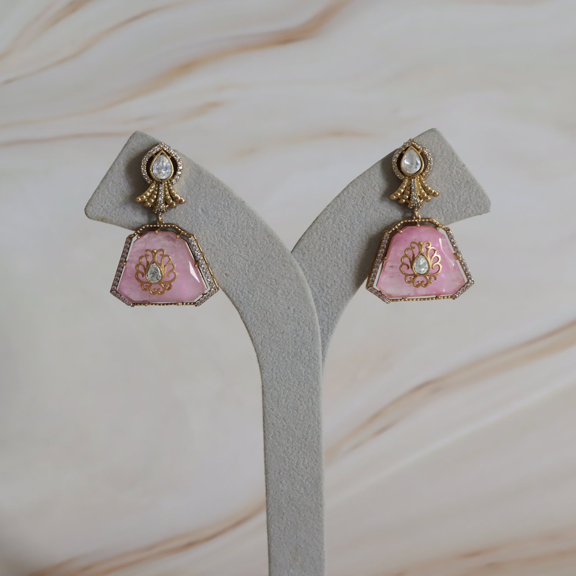 Pair of pink earrings with gold accents on a gray stand against a marble background