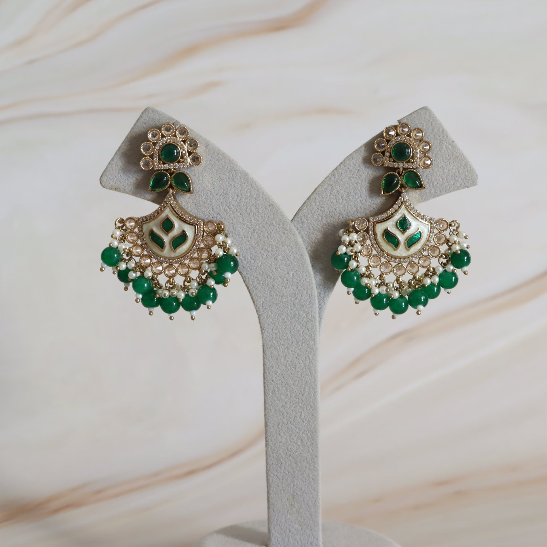 Pair of green and gold earrings on a white stand with a light background