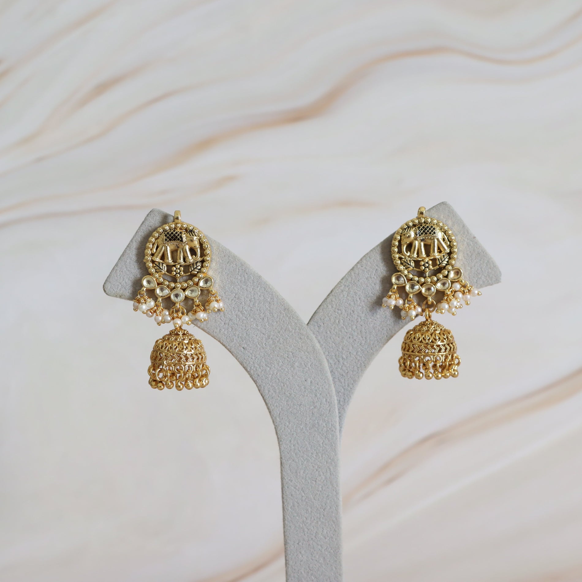 Gold earrings on a white Y-shaped stand with a light background