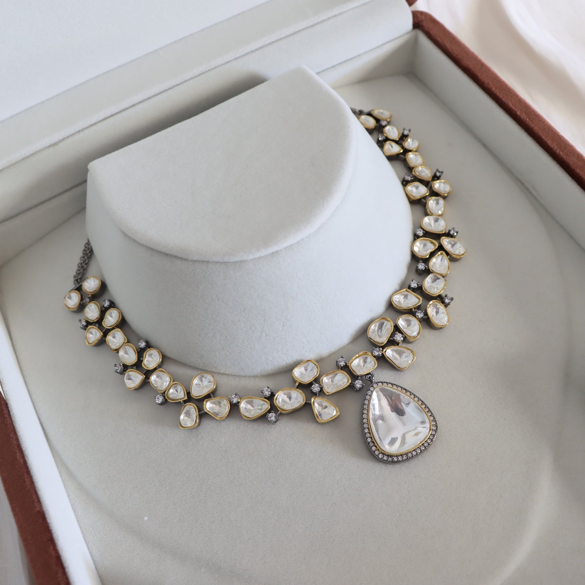 A statement collar necklace with irregular cream-colored pearls and a large teardrop-shaped pearl pendant, set in silver-toned metal, displayed on a white velvet jewelry bust inside an open presentation box.