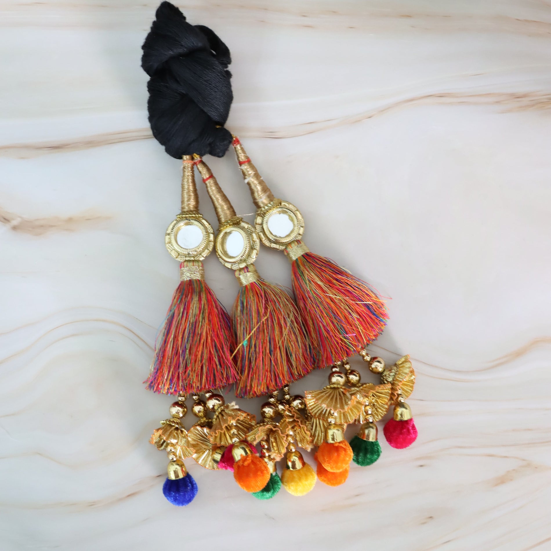 Decorative tassels with colorful pom-poms and gold accents on a light wooden surface.