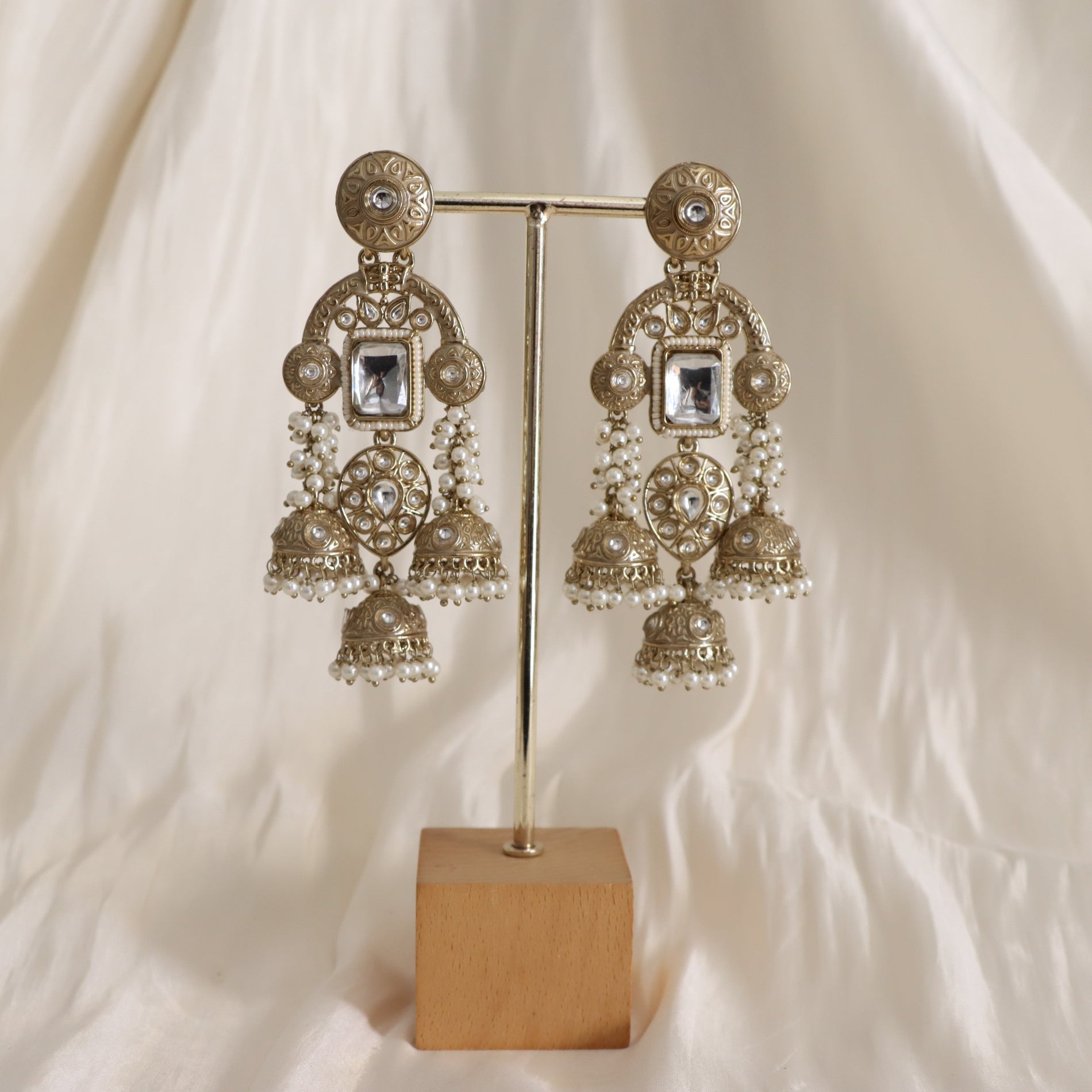 Ornate gold earrings with crystals on a stand against a white background