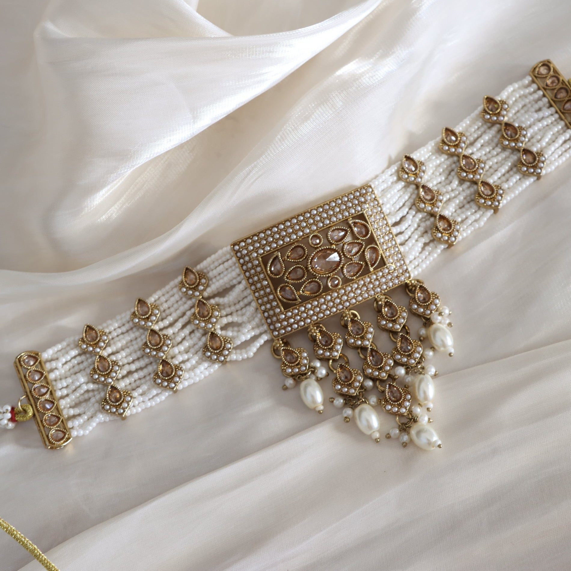 Decorative bracelet with gold and pearl details on a white fabric background