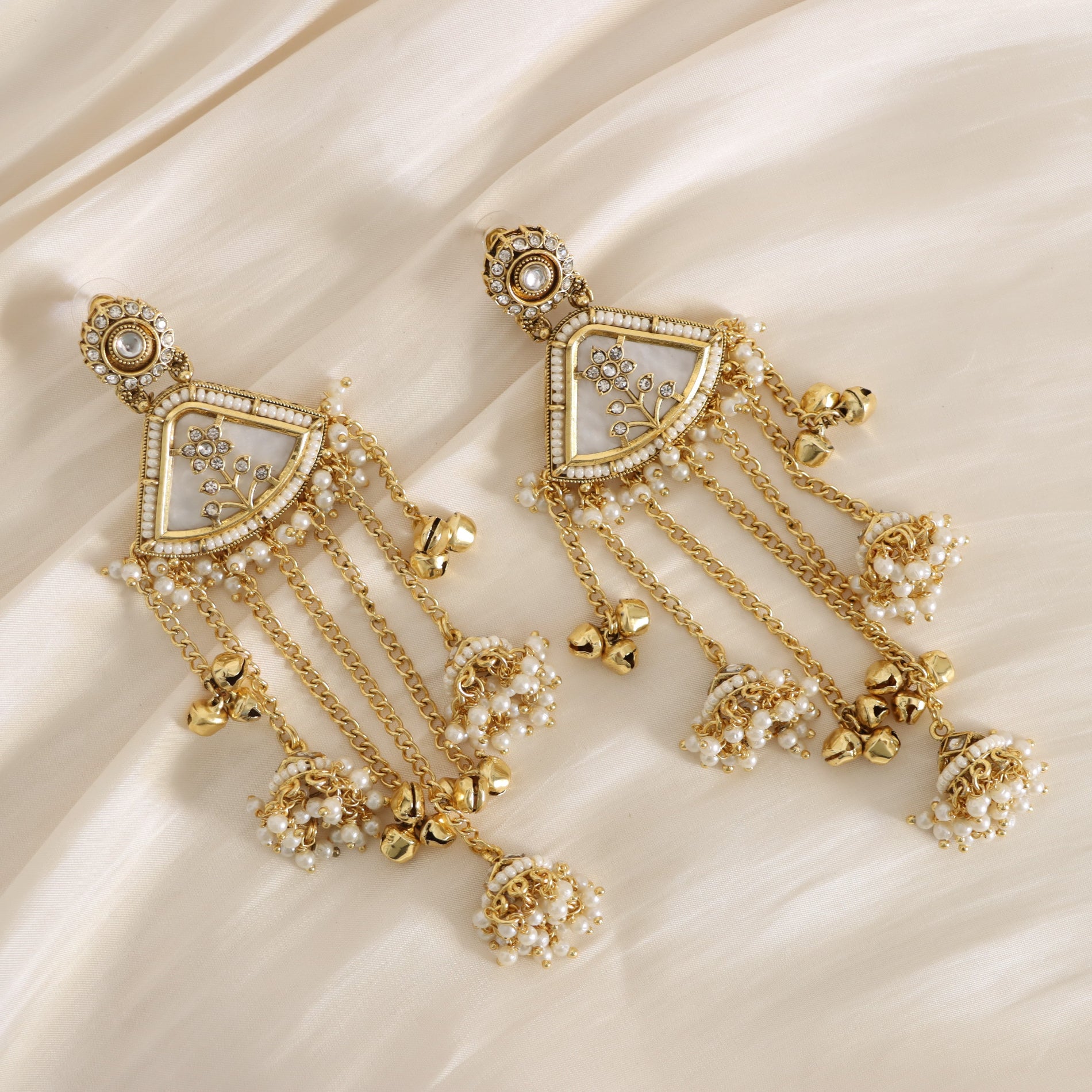 Pair of gold earrings with pearl-like stones on a beige fabric background