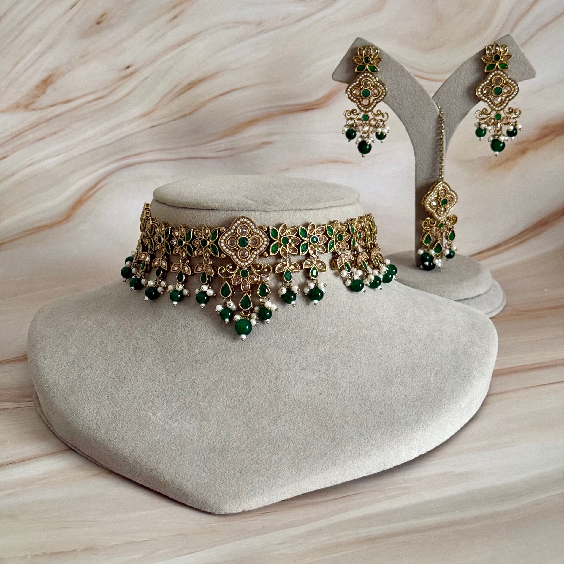 Gold and green jewelry set on a marble surface