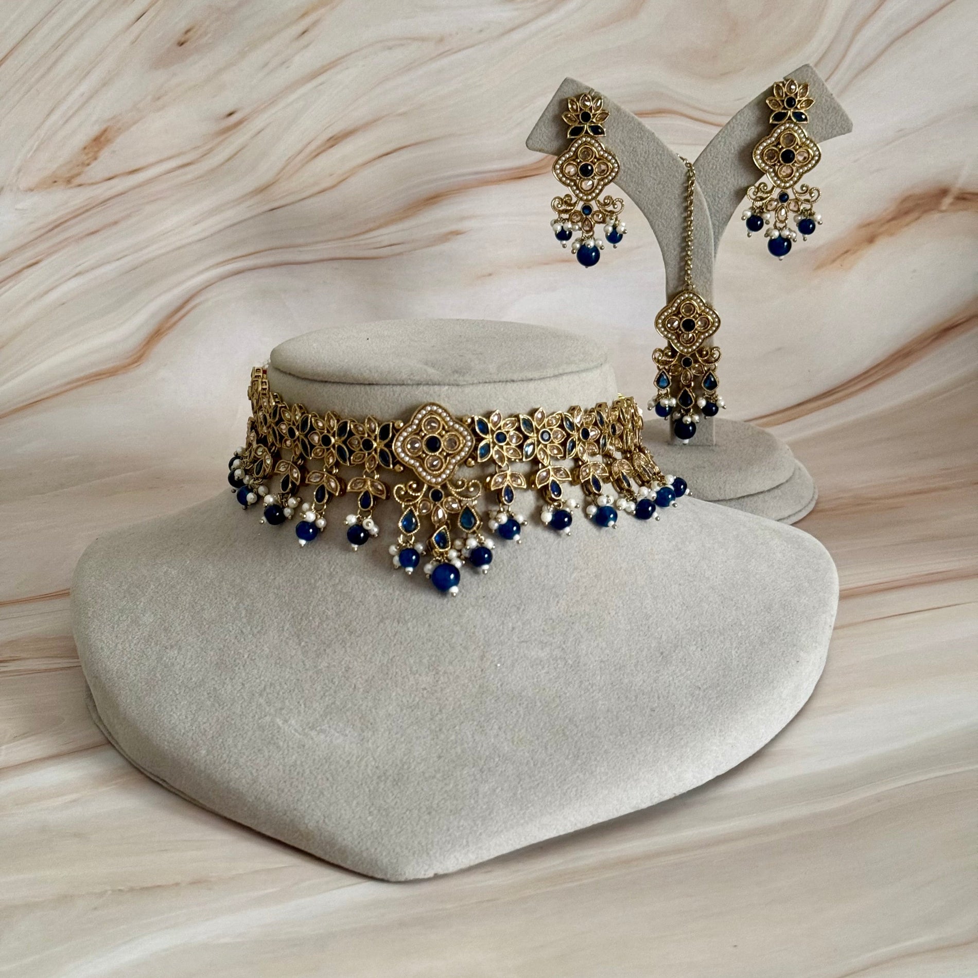 Gold and blue jewelry set on a gray stand with a marble background