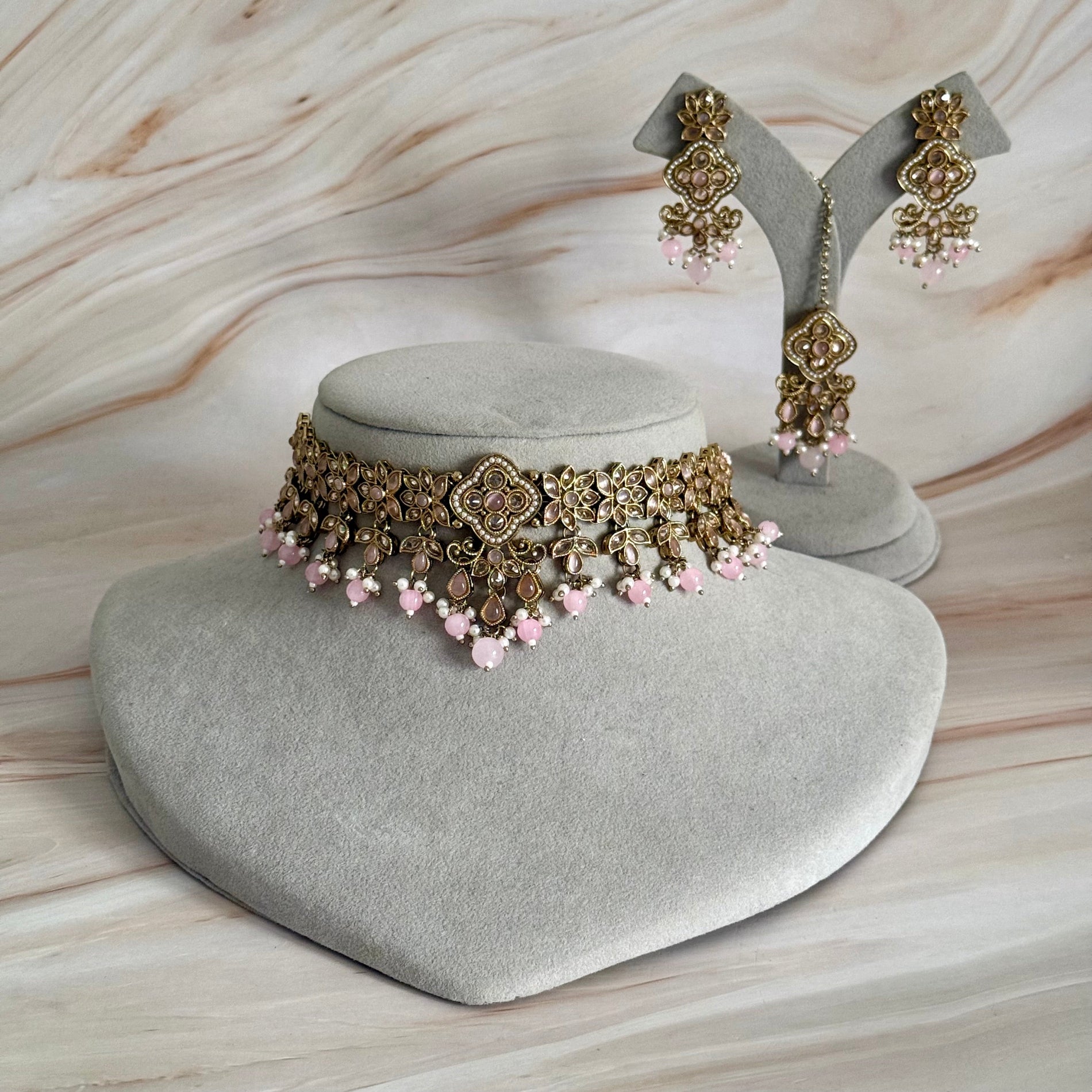 Jewelry set with choker and earrings on a gray cushion against a marble background