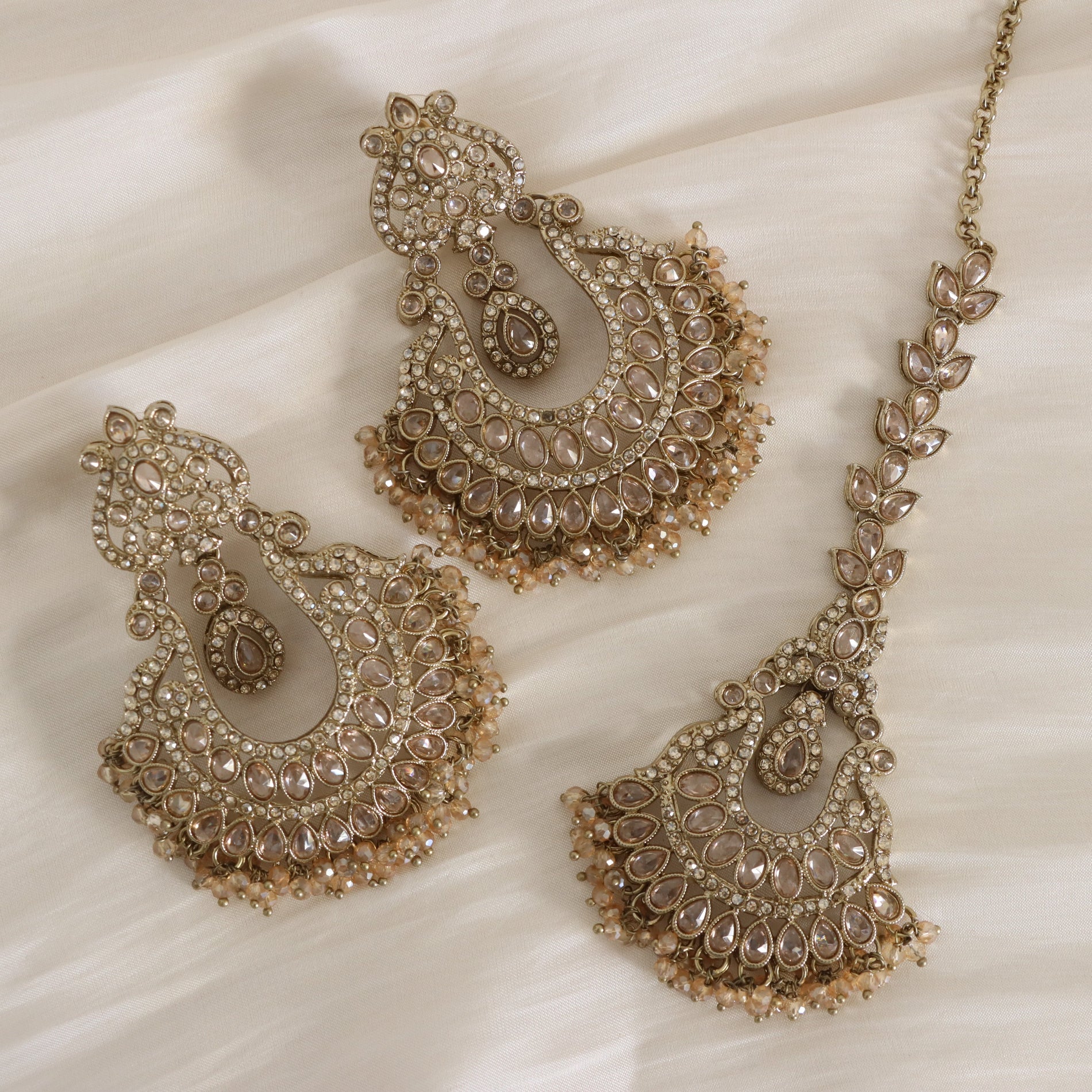 Ornate gold necklace with matching earrings on a white fabric background