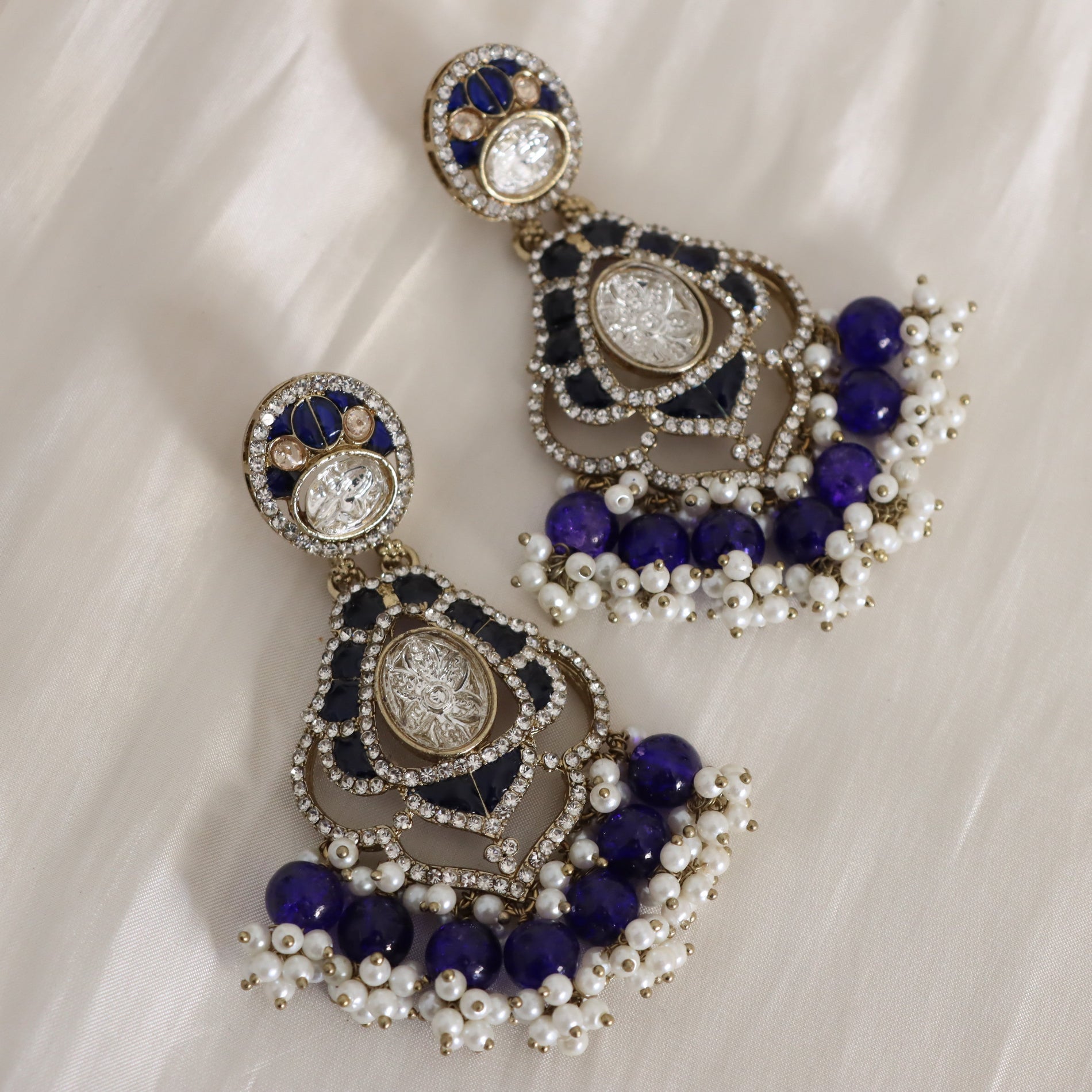 Ornate earrings with blue and white beads on a white fabric background