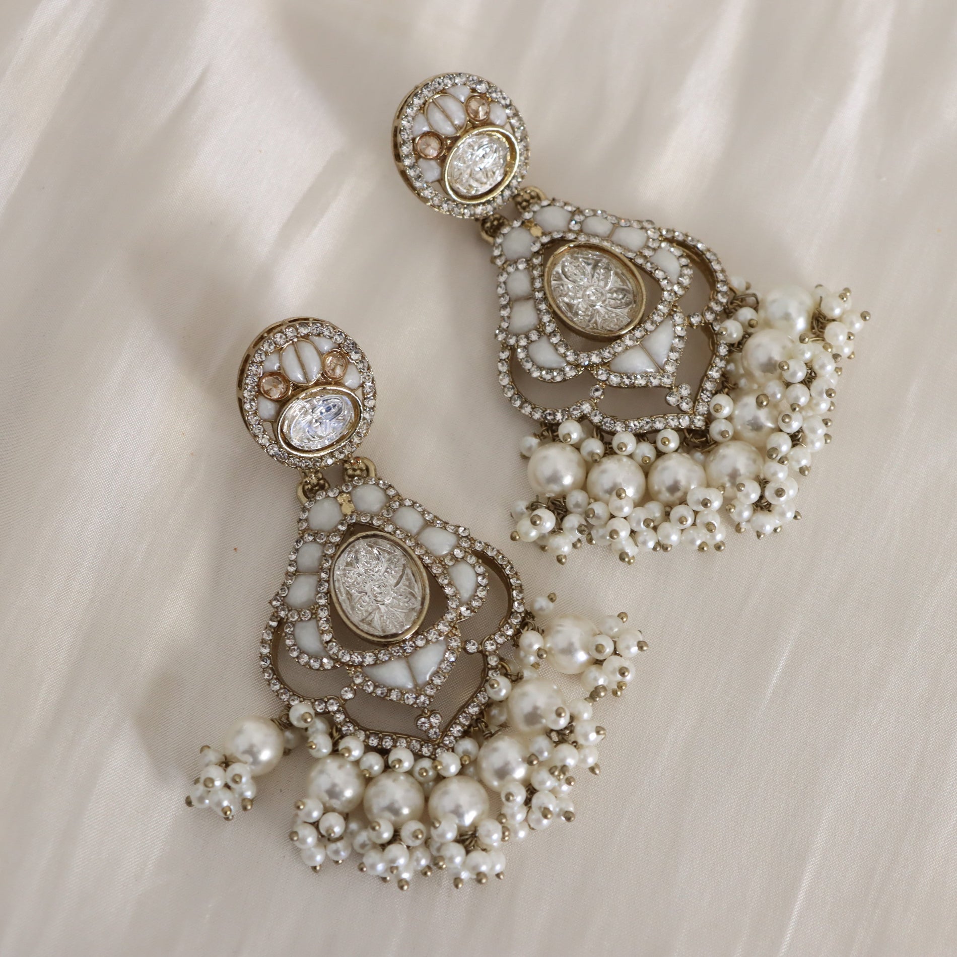 Pair of ornate earrings with pearls and gemstones on a soft fabric background