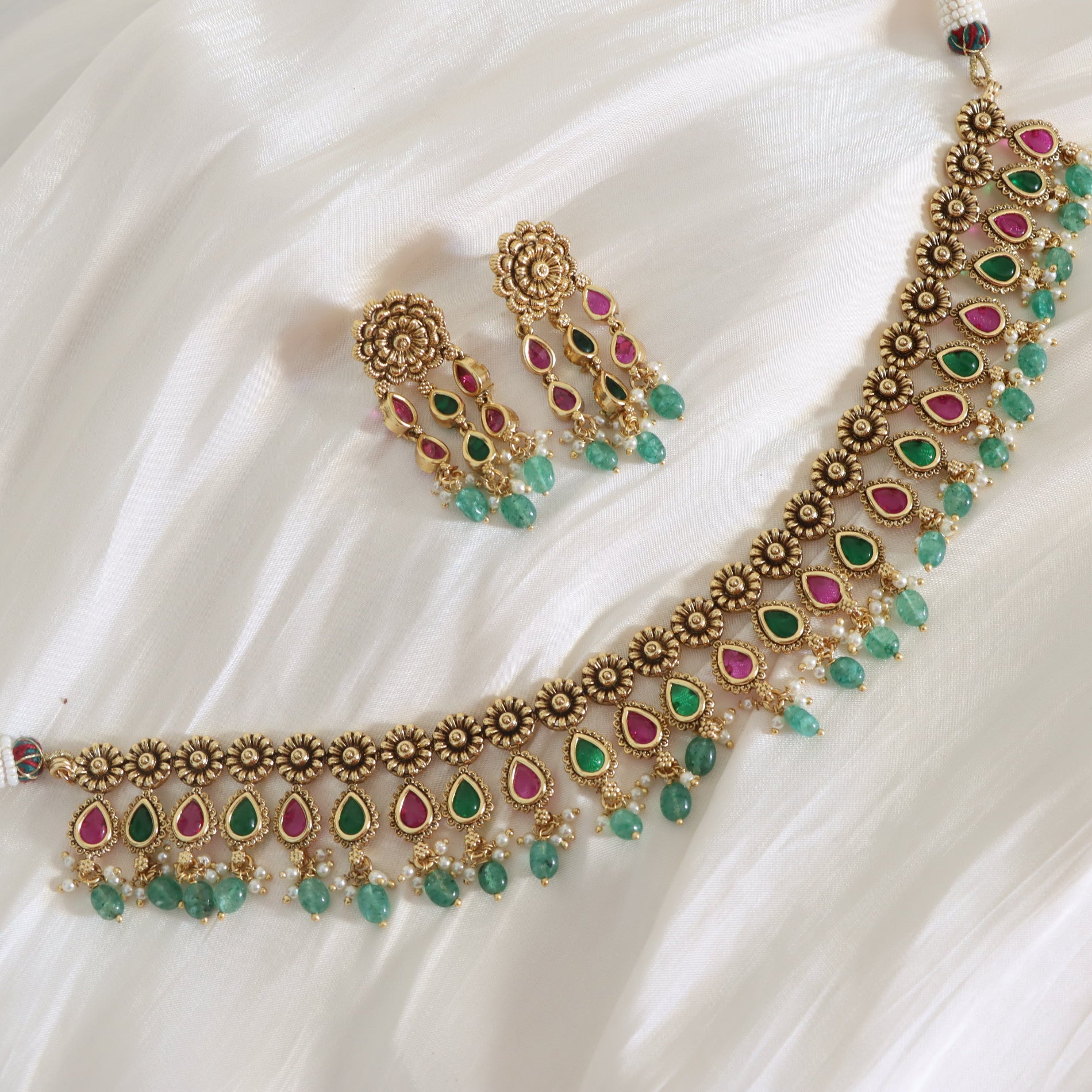 Ornate necklace with green and pink stones on a white fabric background