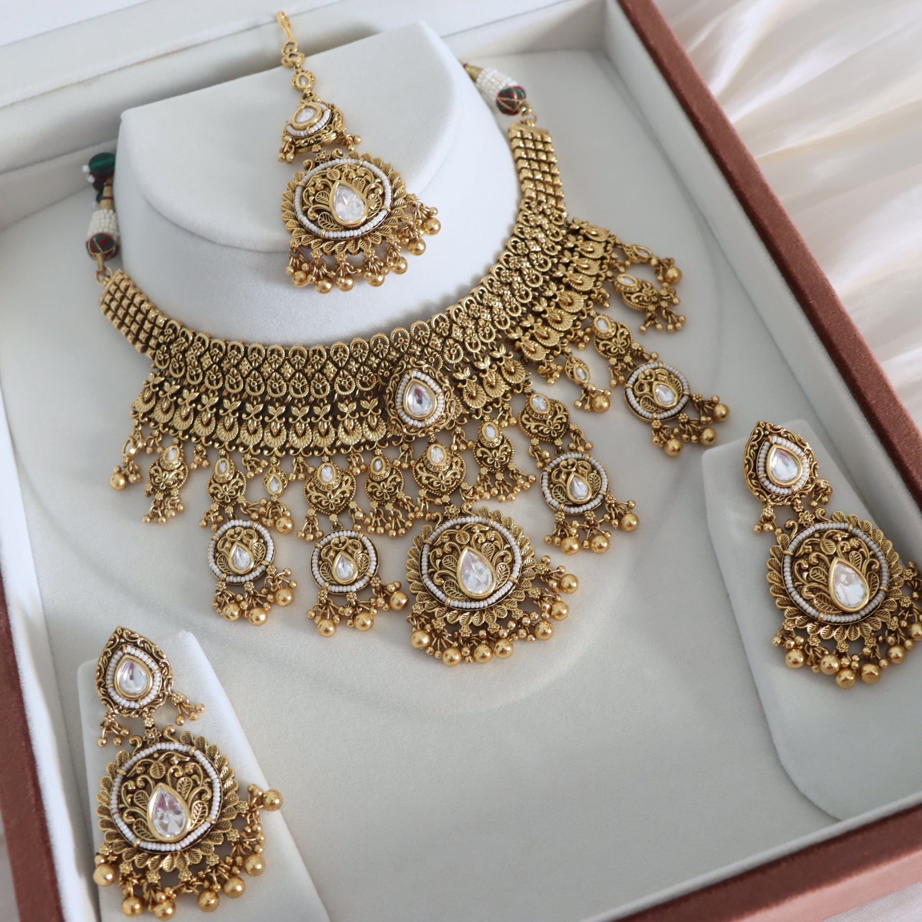 Gold necklace and earrings set on a white stand with a pink box in the background