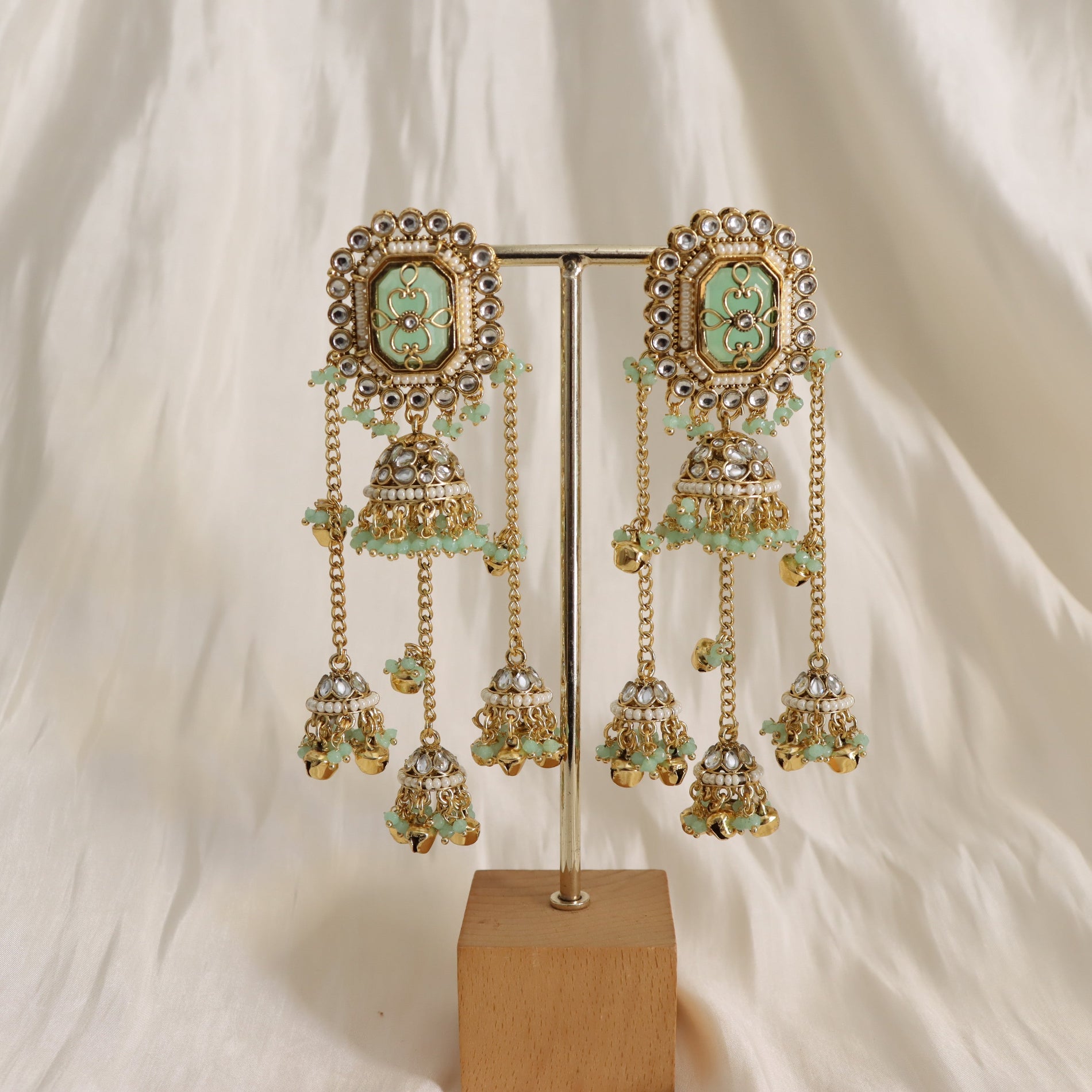 Ornate earrings with green gemstones on a stand against a white background
