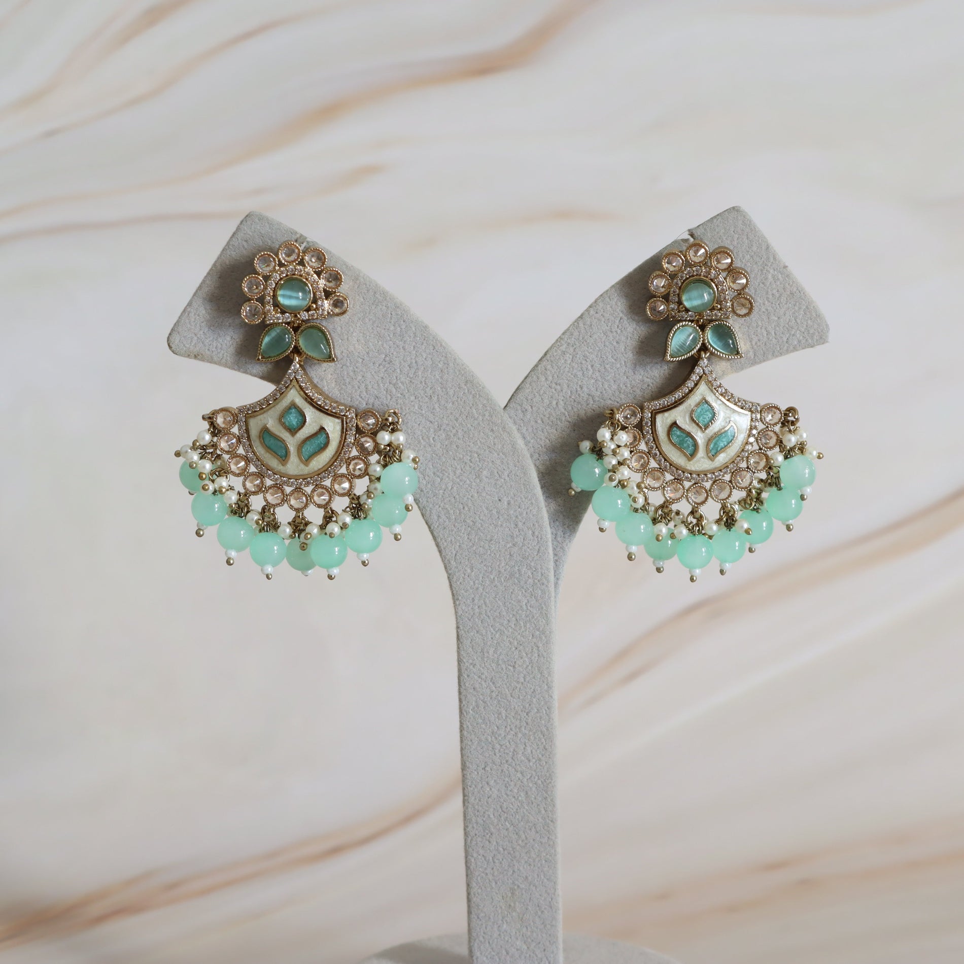 Pair of earrings with turquoise stones on a white stand against a marble background
