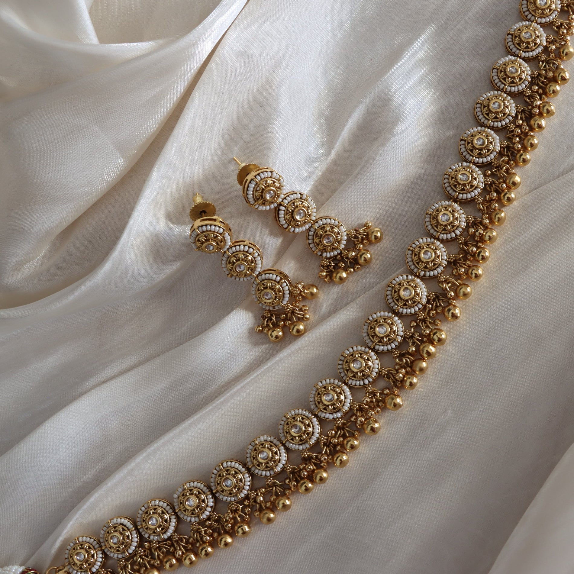 Gold necklace and earrings on a white fabric background
