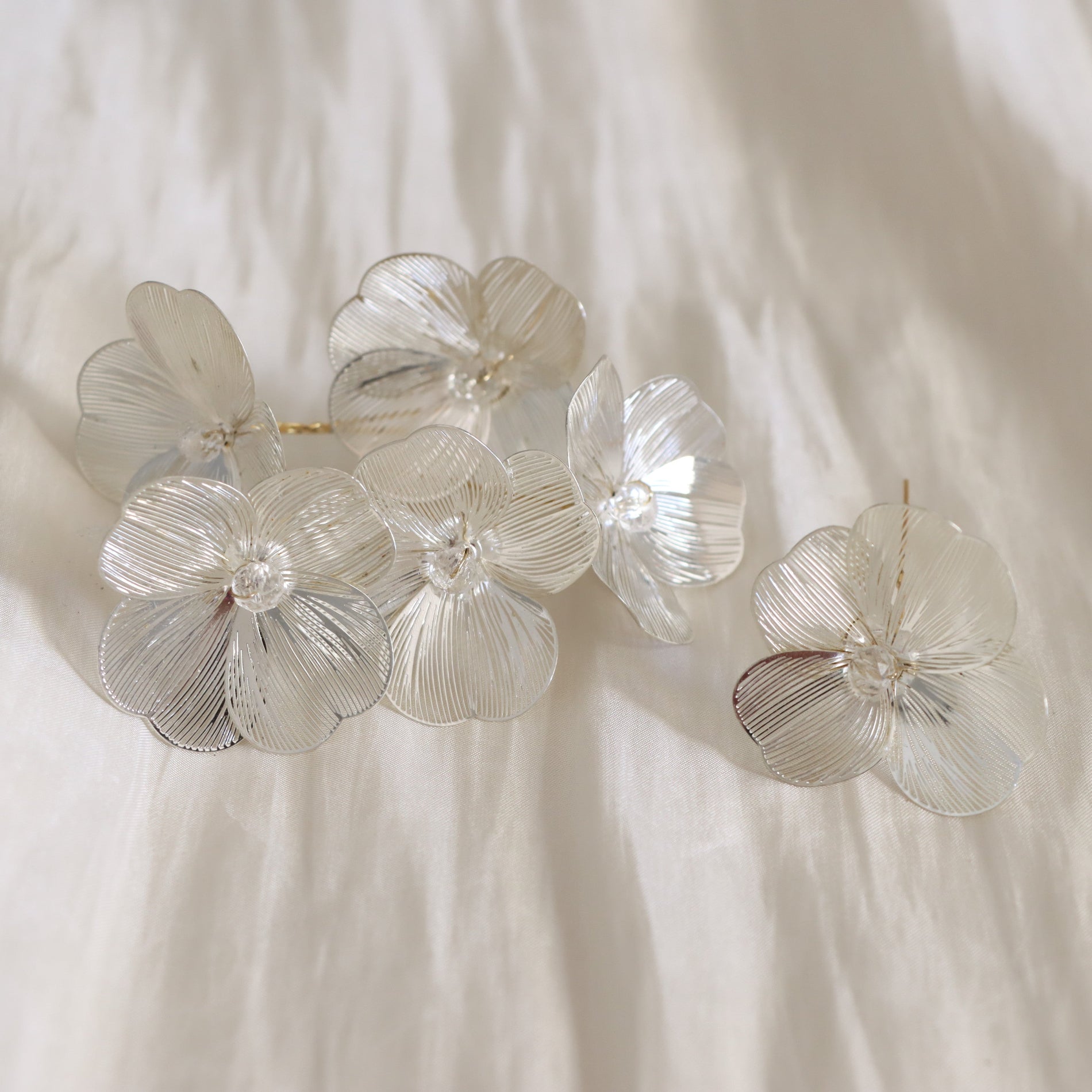 A set of five clear, flower-shaped hair clips with textured petal details and gold-tone metal backing, arranged on a soft, off-white fabric background.