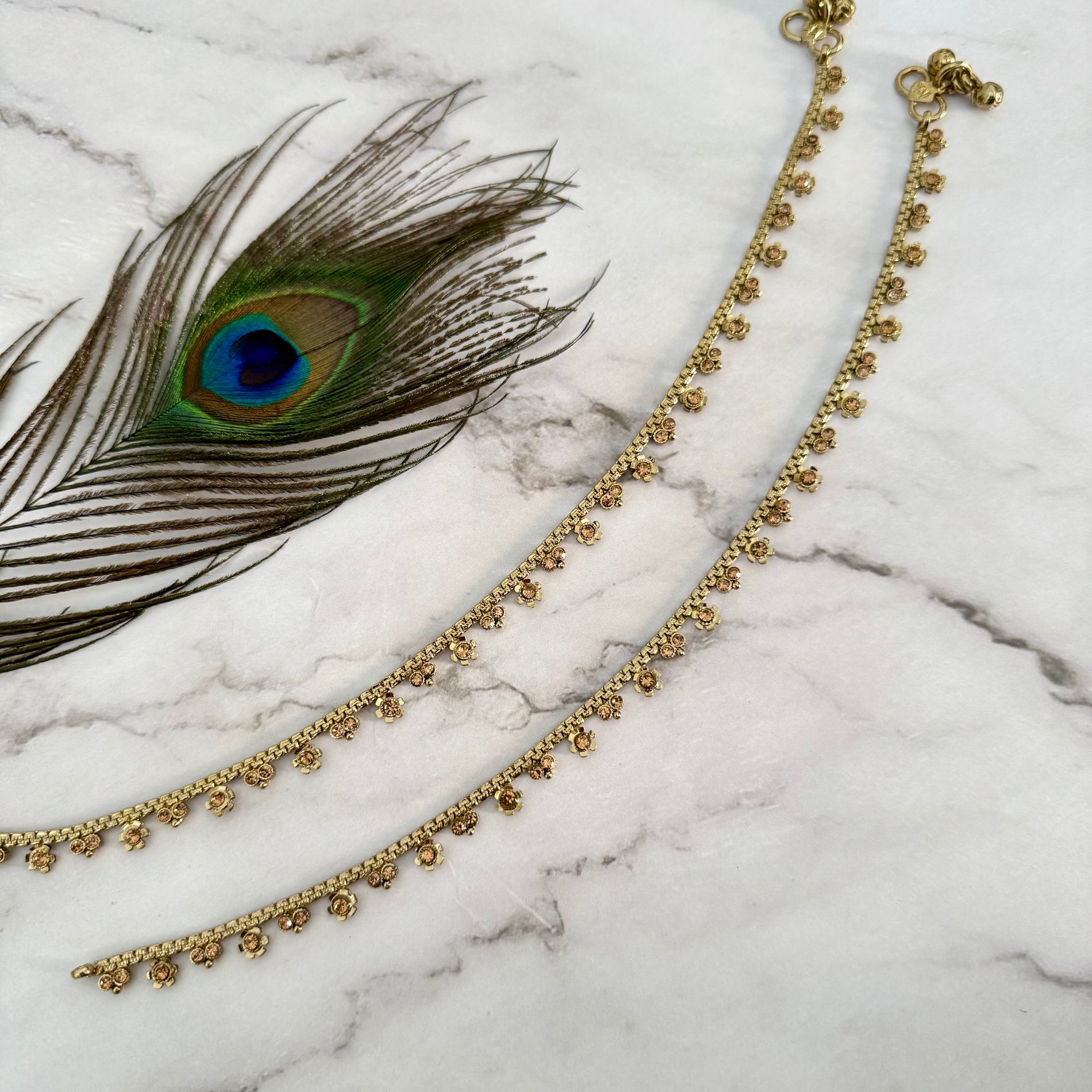 Gold anklet with peacock feather on marble surface