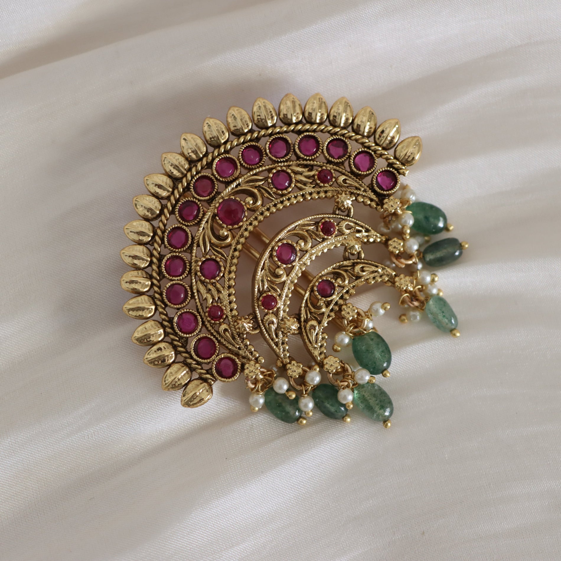 Decorative brooch with gold, red, and green stones on a white fabric background