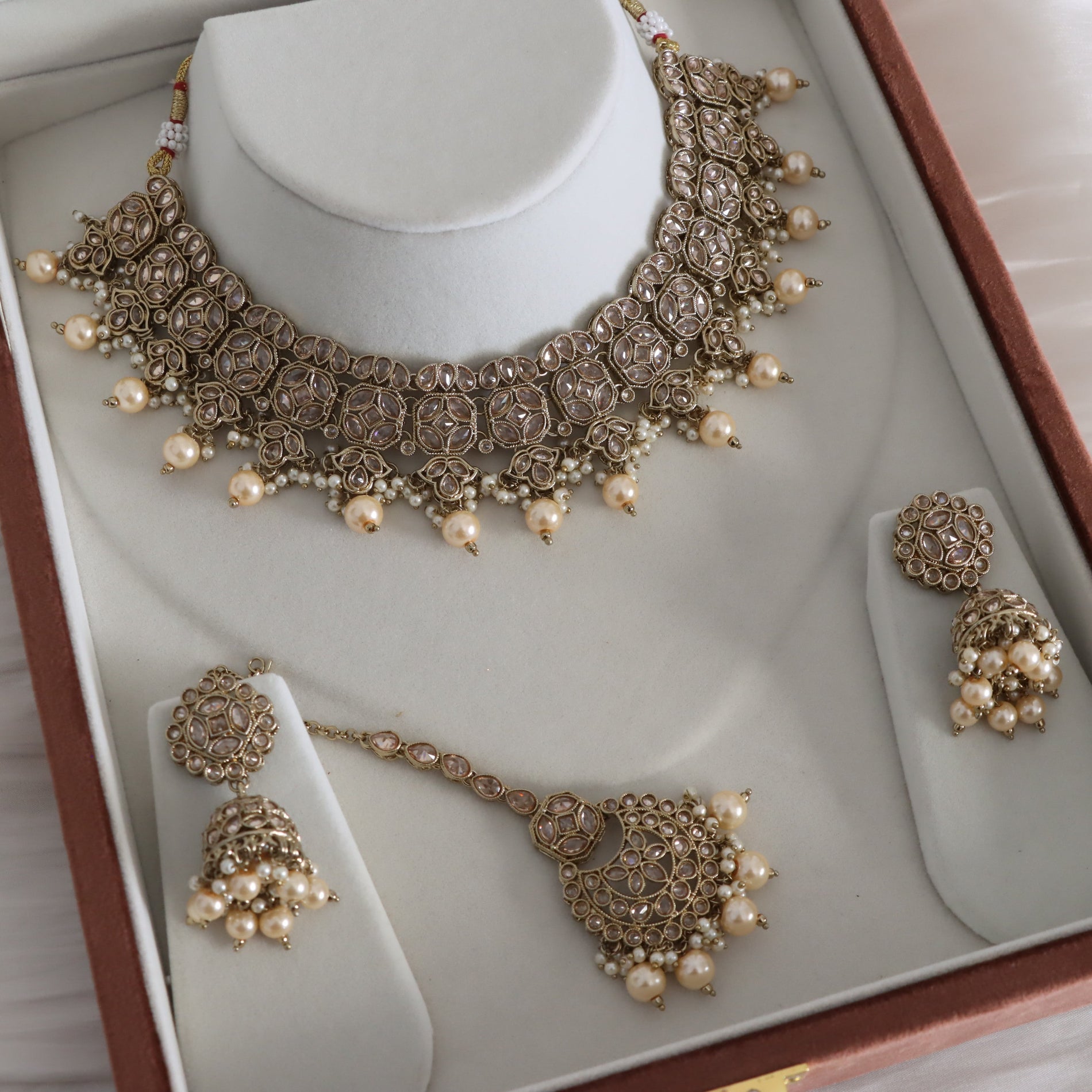 Ornate jewelry set with necklace, earrings, and bracelet on a white display stand.