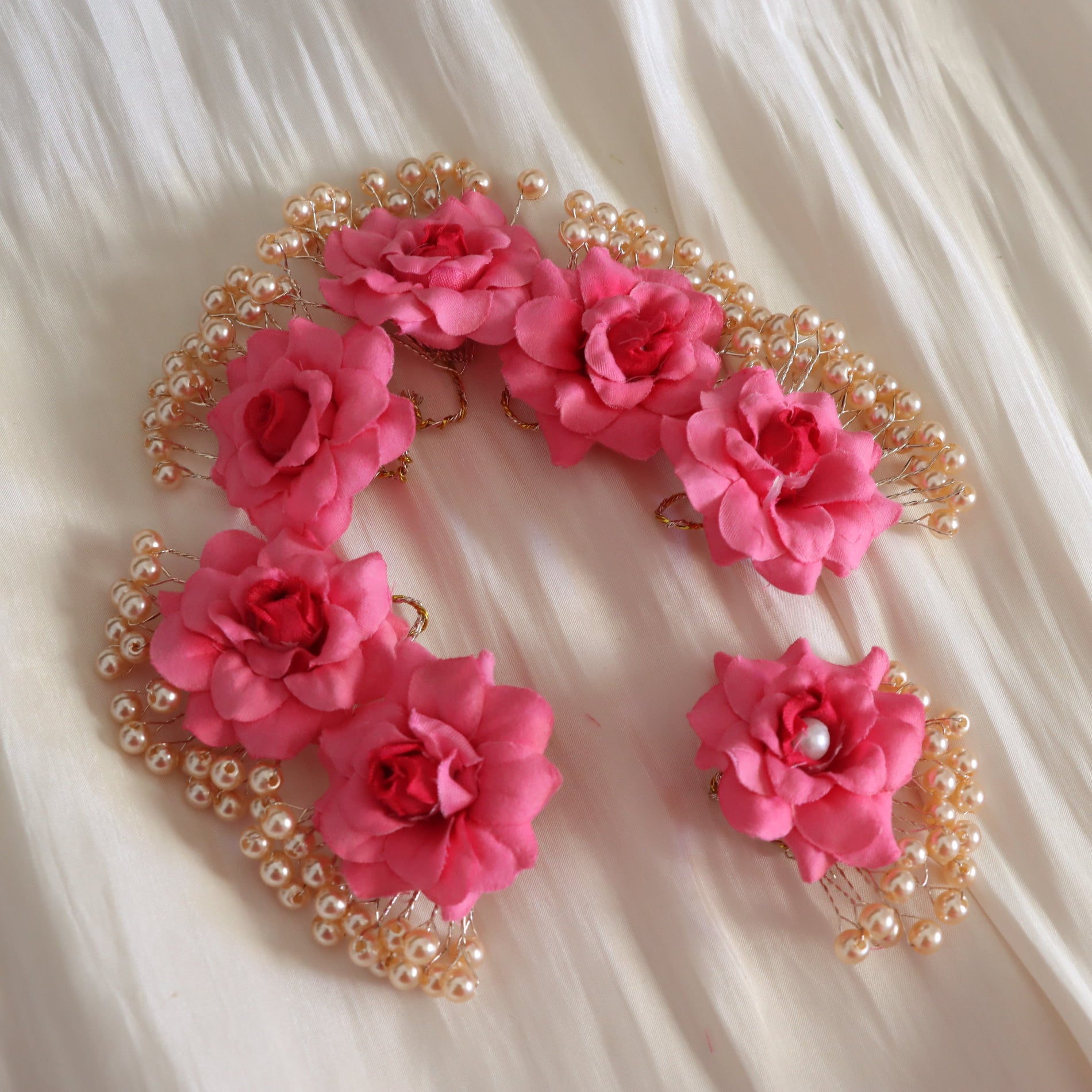 Three pink fabric rose hair accessories with pearl bead borders, arranged on a white satin fabric background.