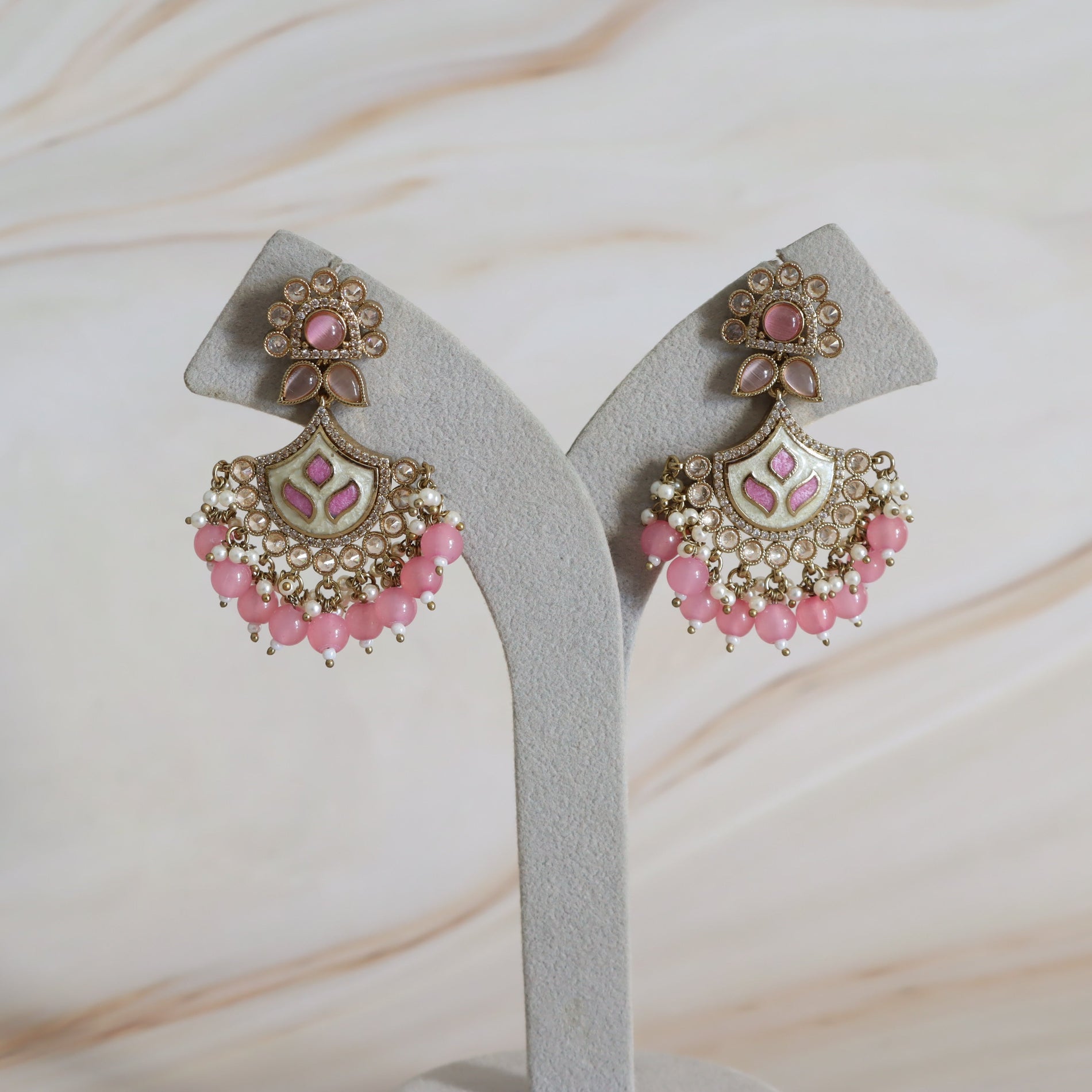 Pair of pink and gold earrings on a white stand with a marble background