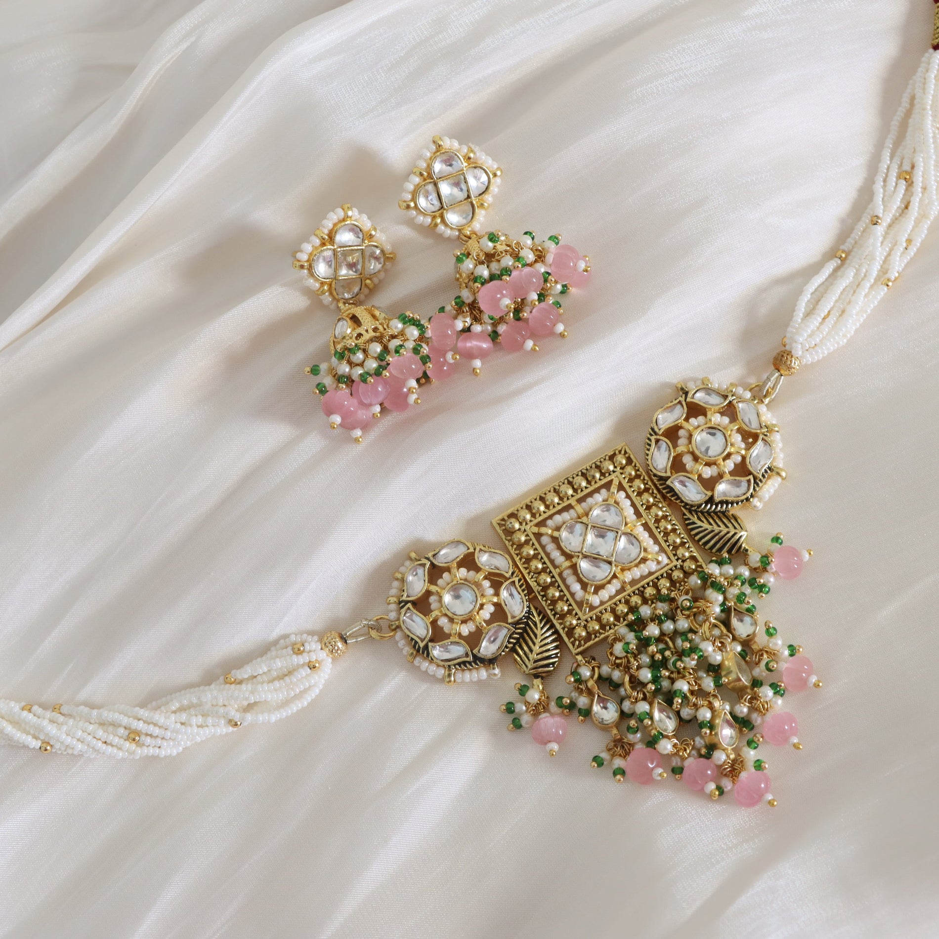 Ornate necklace and earrings with pink and green stones on a white fabric background