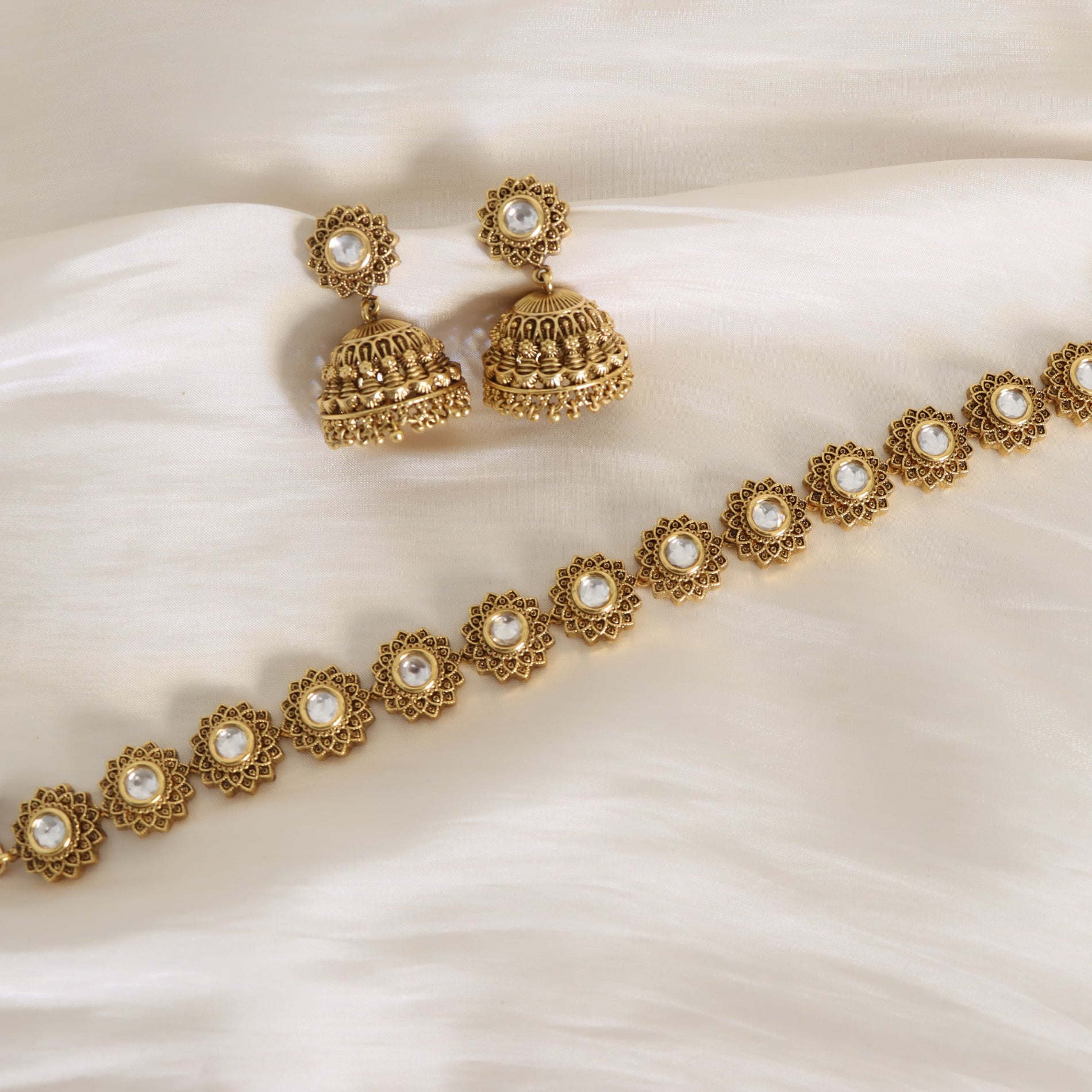 Gold jewelry set with earrings and a bracelet on a white fabric background