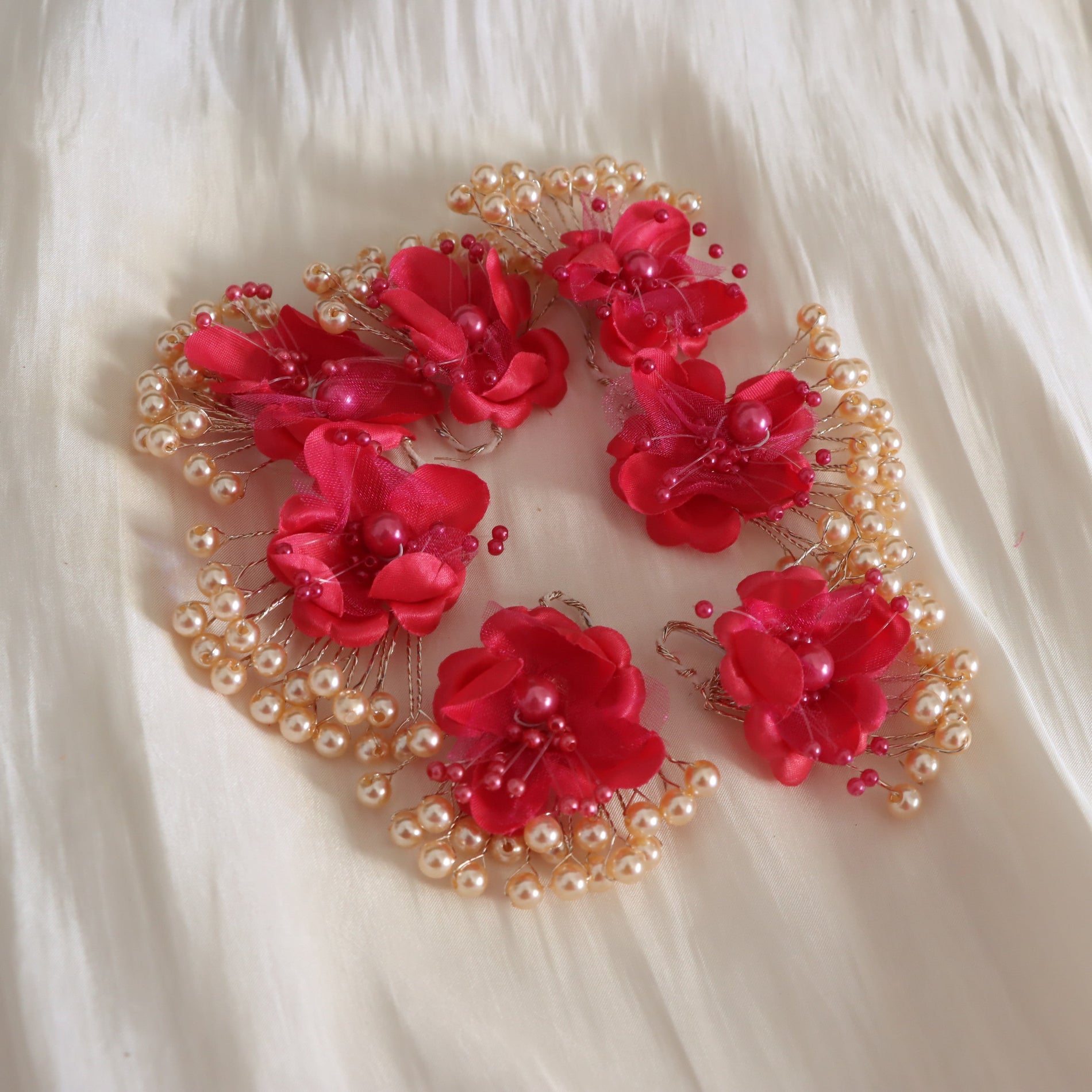 A decorative embroidered headpiece or hair accessory featuring five bright red fabric flowers with pearl-like beads and gold-toned wire details, arranged on a soft white fabric background.