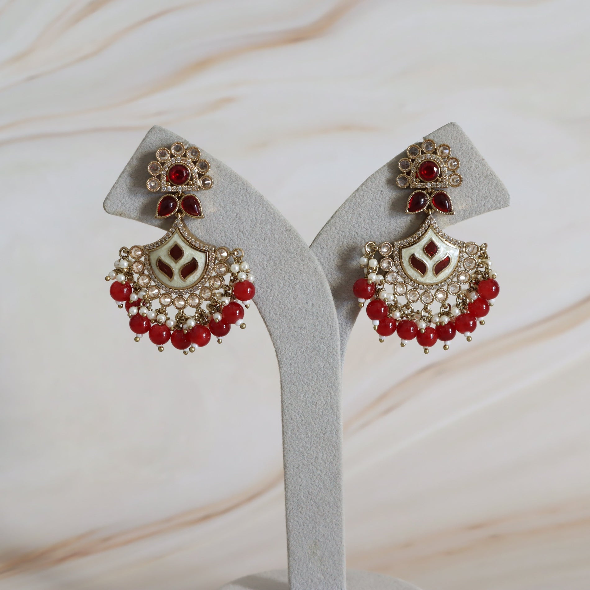 Pair of ornate earrings with red stones on a white stand against a marble background