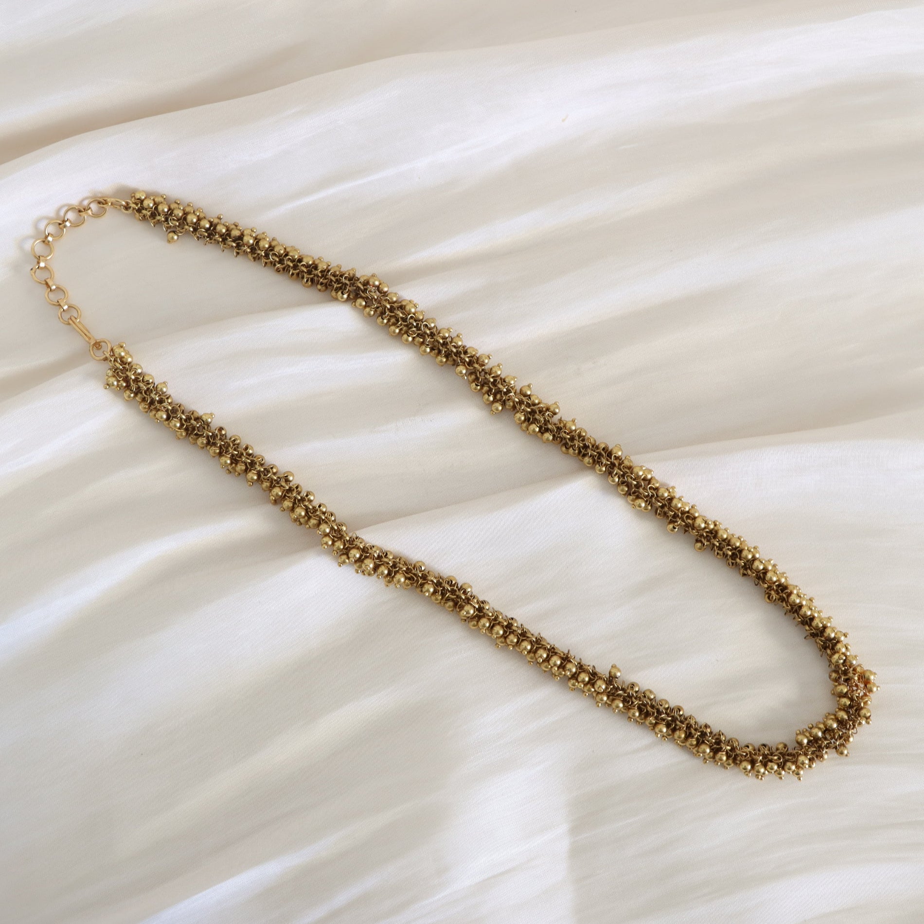 Gold beaded necklace on a white fabric background