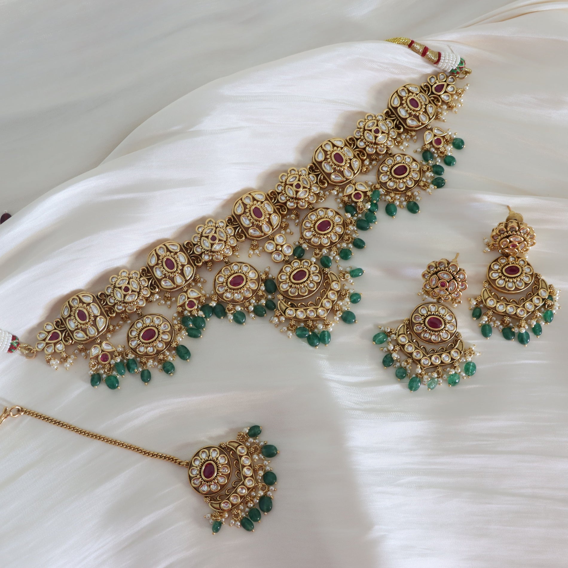 Ornate gold necklace with red and green gemstones on a white fabric background