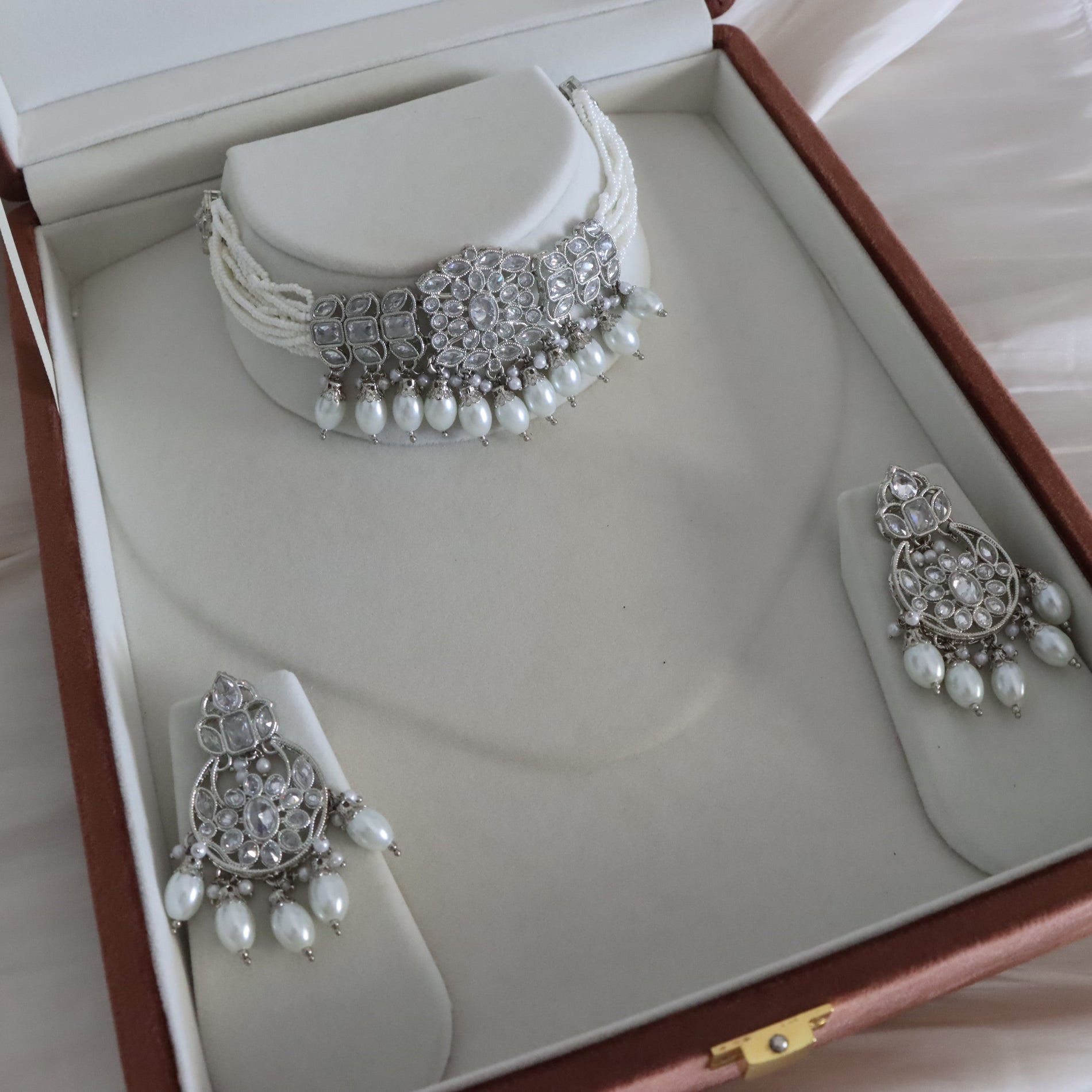 A silver-toned jewelry set displayed inside an open presentation box, featuring a choker necklace with pearl-like drops and matching drop earrings with clear stones and white pearl accents.