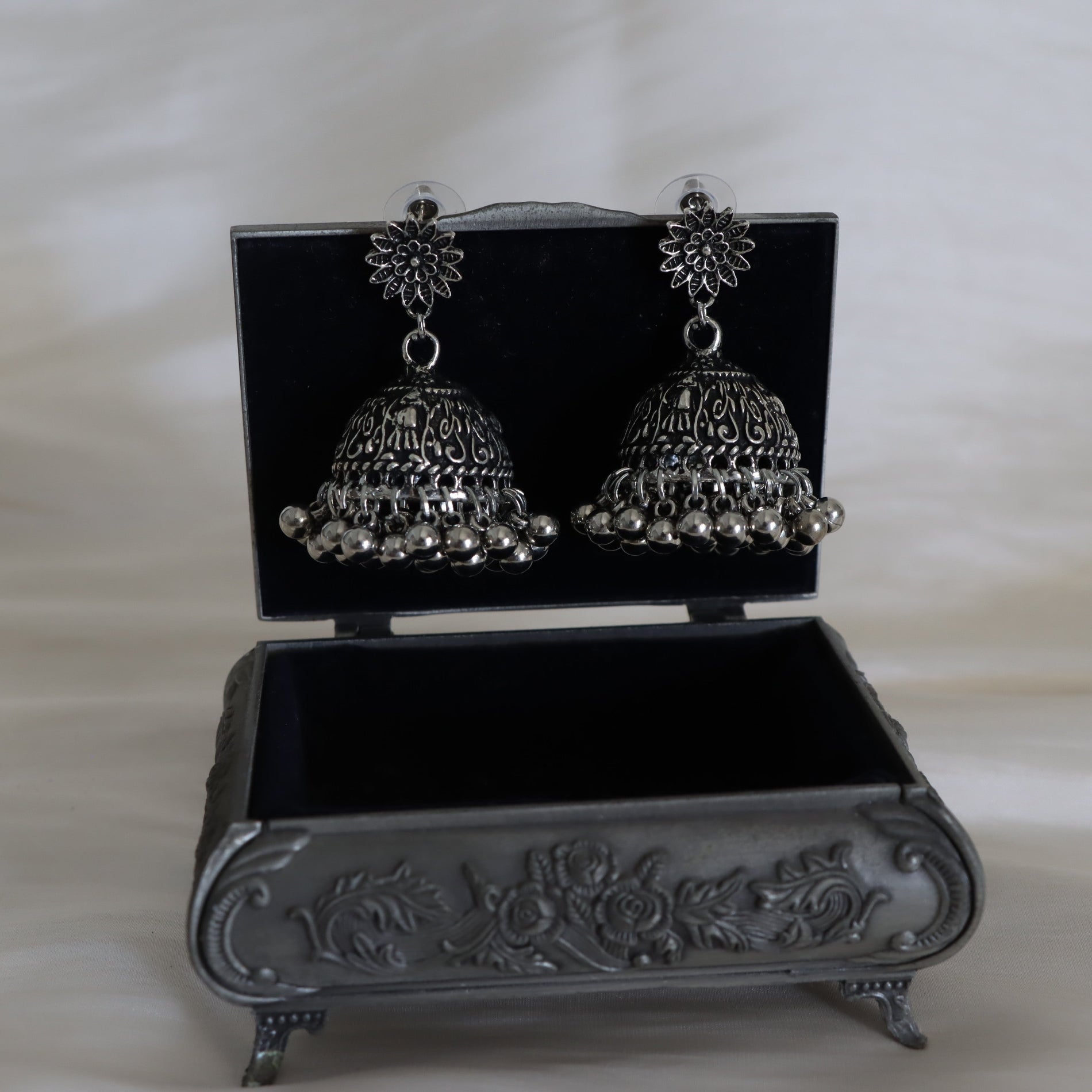Silver jhumka earrings in an ornate black jewelry box on a white background