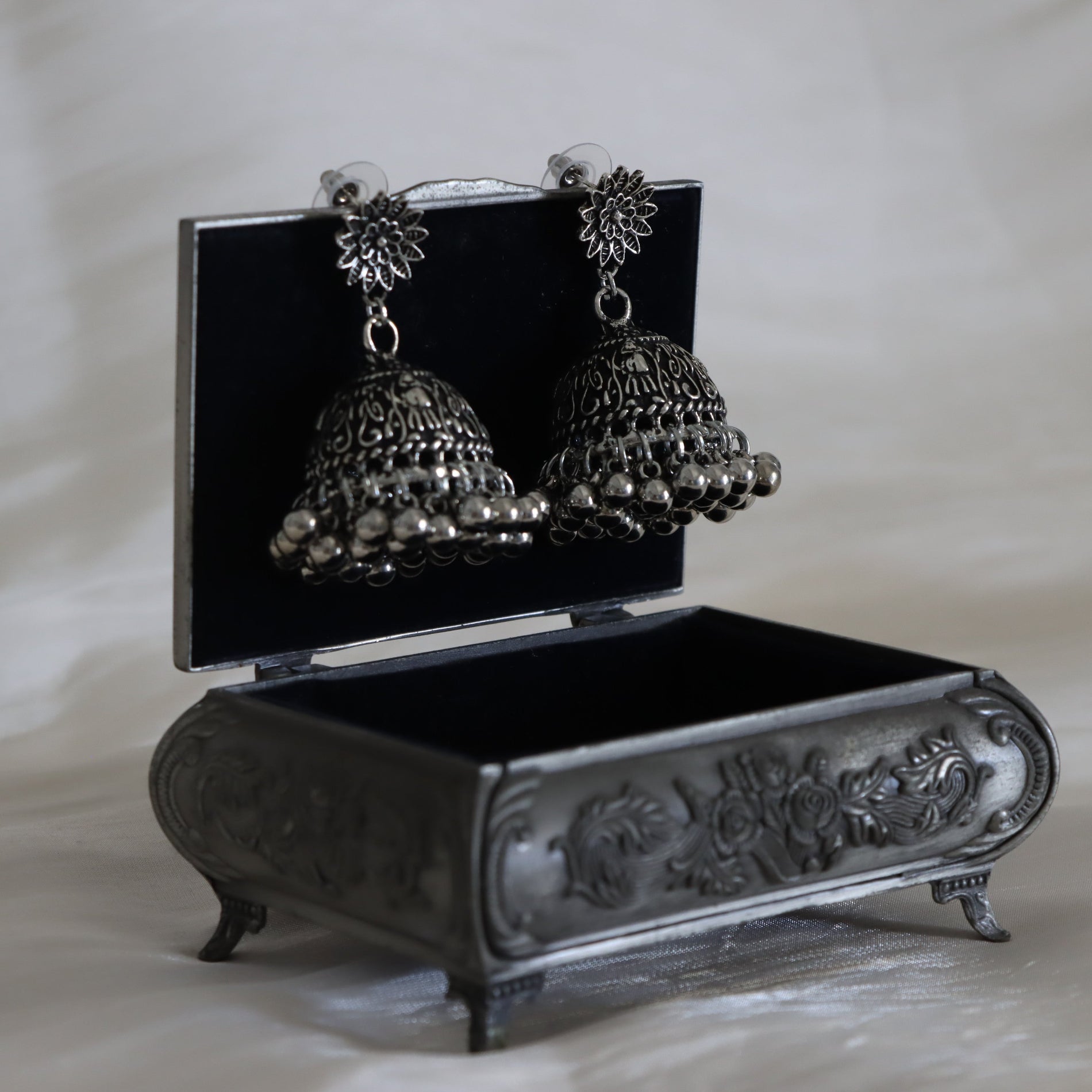 Pair of silver jhumka earrings on a decorative black stand with floral designs.