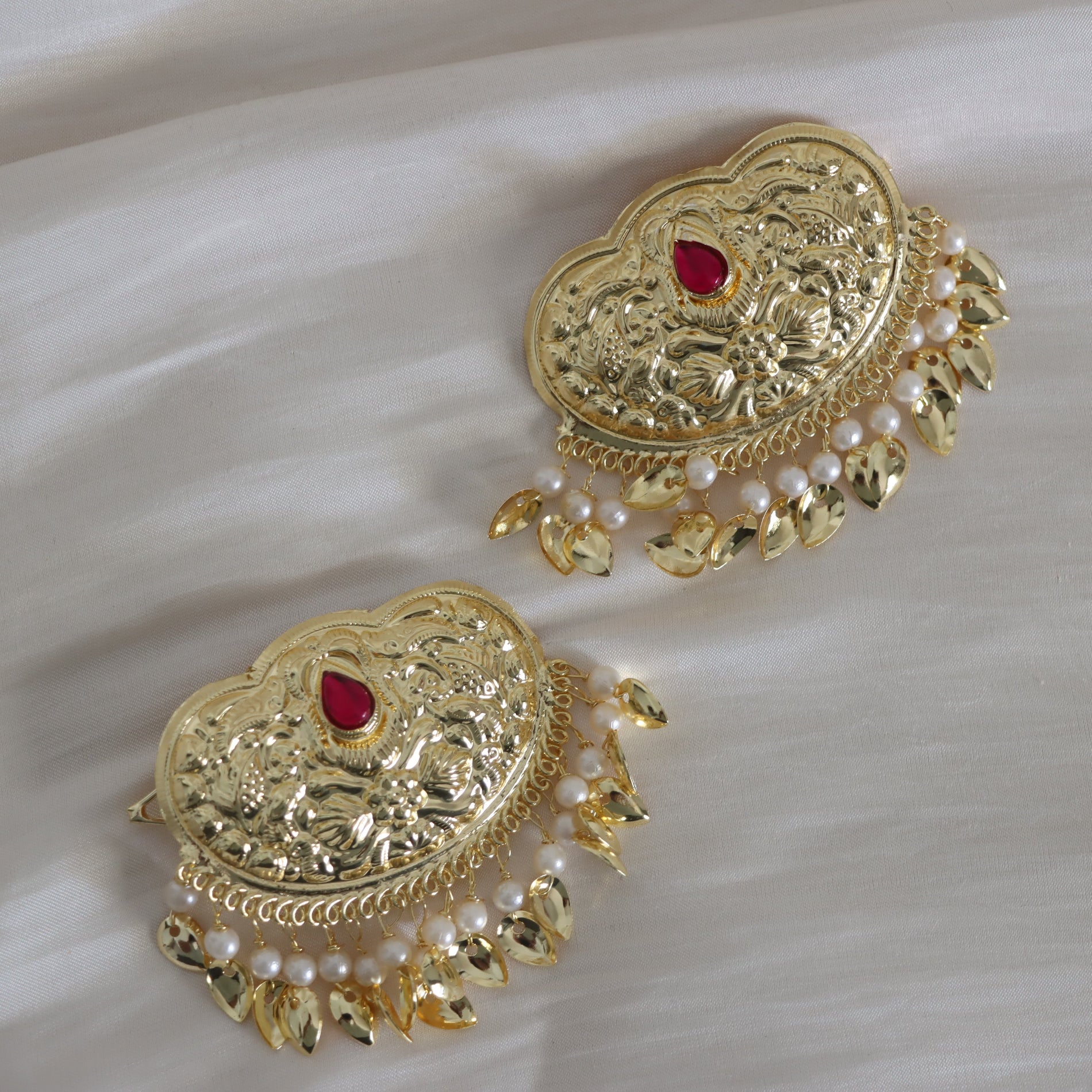Gold hair clip with red stones and pearl-like beads on a white fabric background
