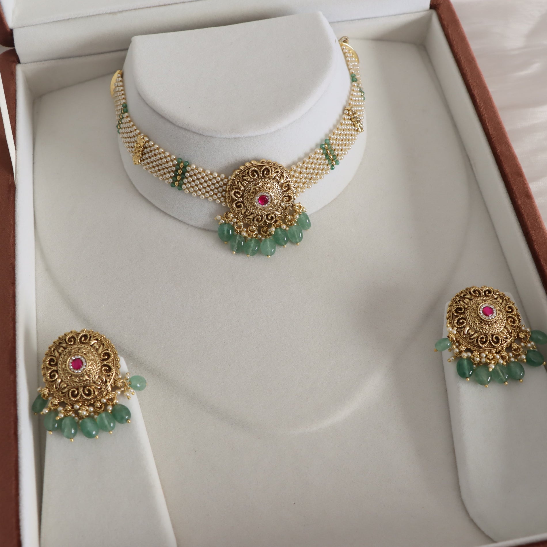 Gold and green beaded jewelry set displayed in an open presentation box, including a necklace on a stand and two matching earrings on display stands.