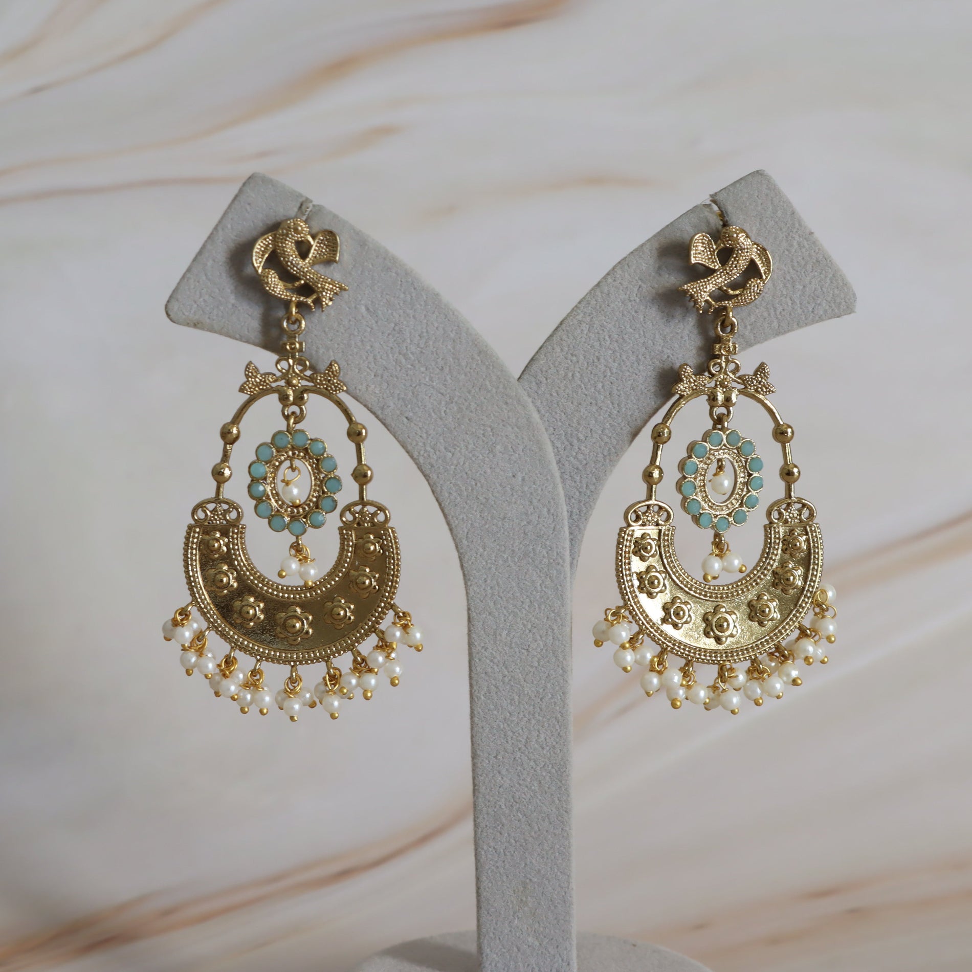 Pair of gold and turquoise earrings on a gray stand with a soft background