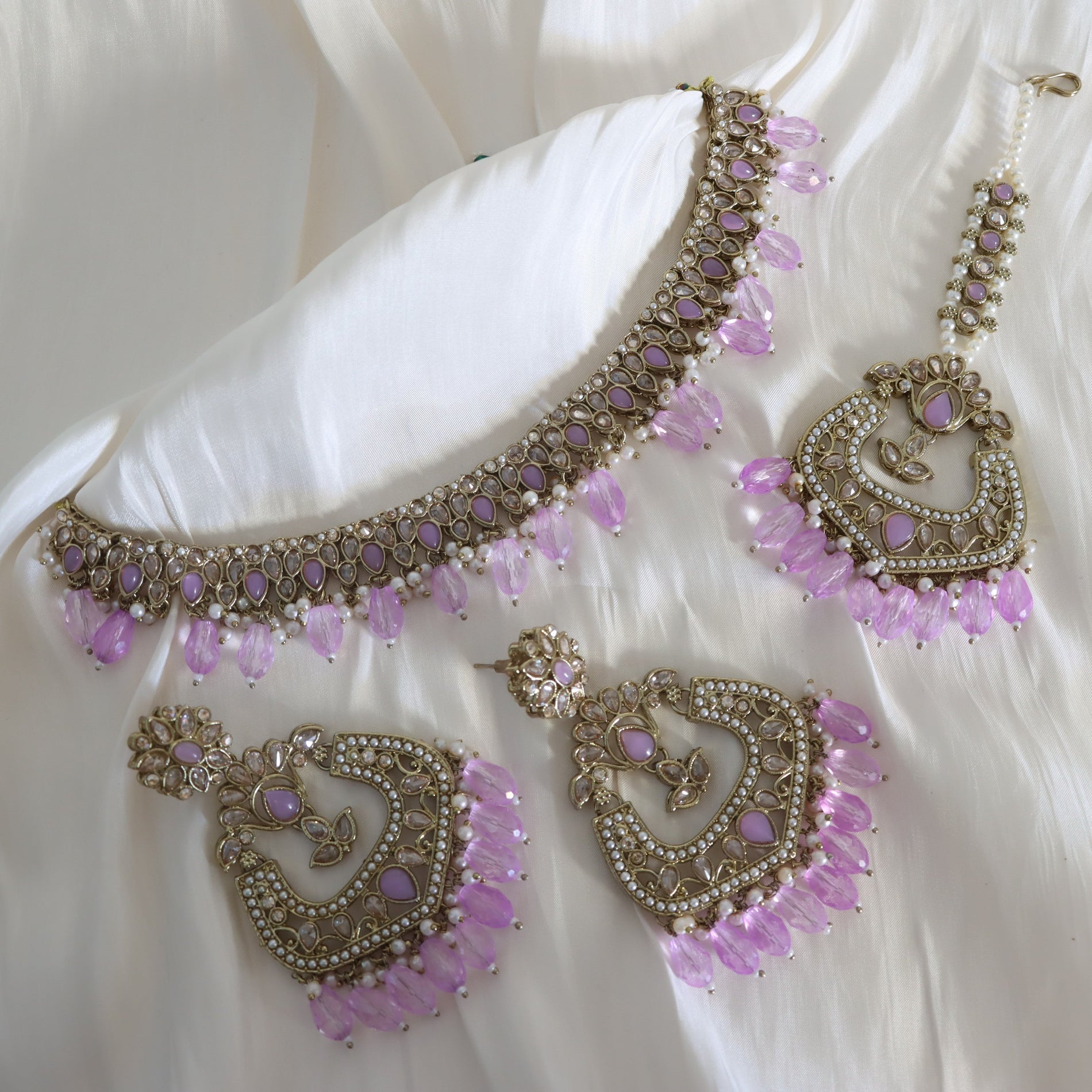 Ornate necklace and earrings with pink stones on a white fabric background